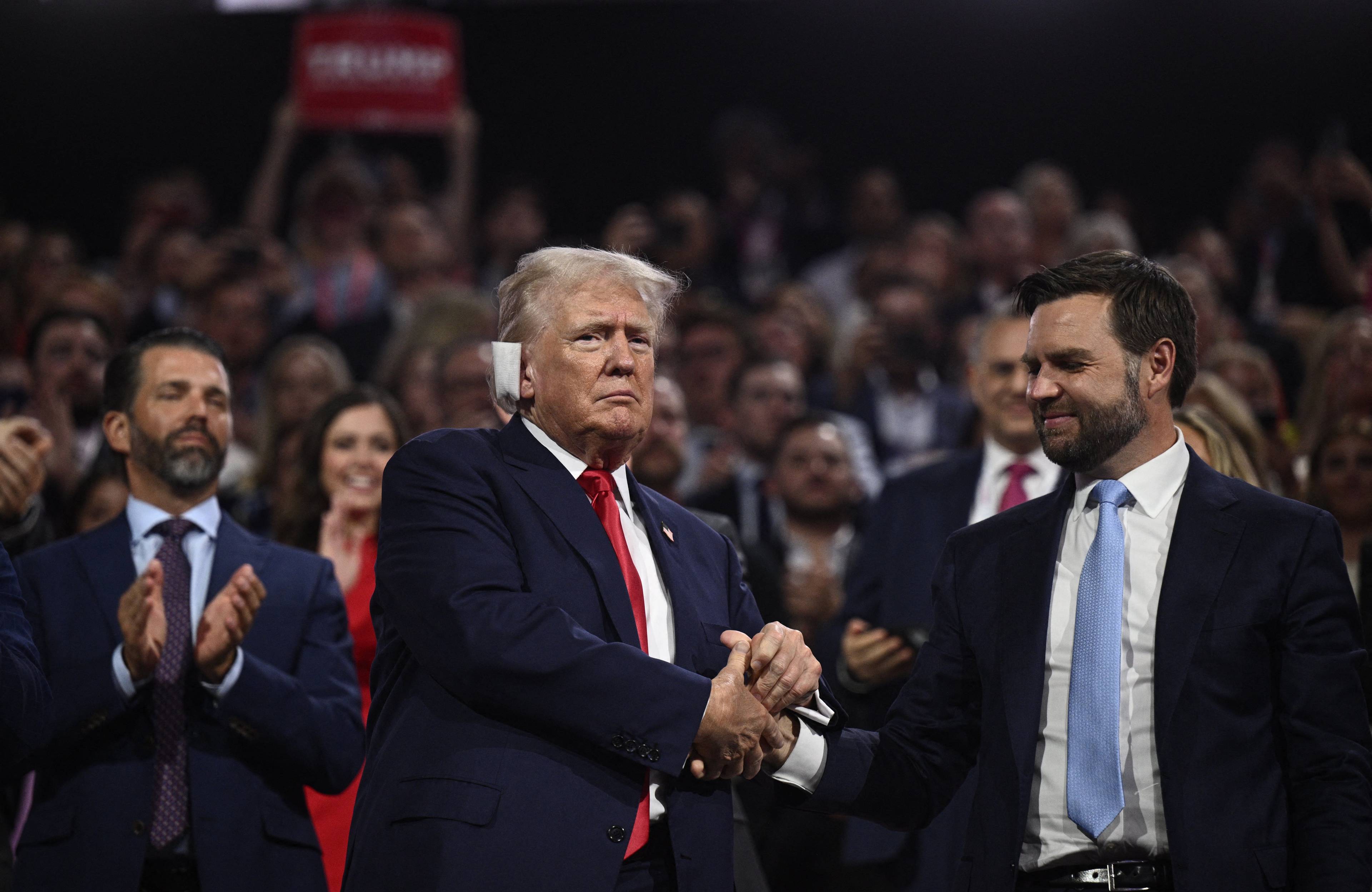 Dwóch mężczyzn (Donald Trump i James David Vance) stoi obok siebie, ściskając sobie ręce, w tle publiczność