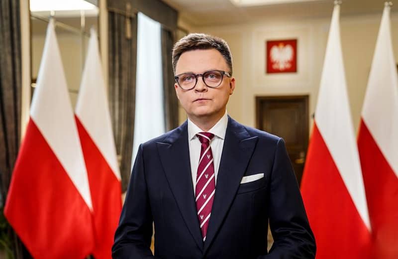 Szymon Hołownia na tle biało-czerwonych flag