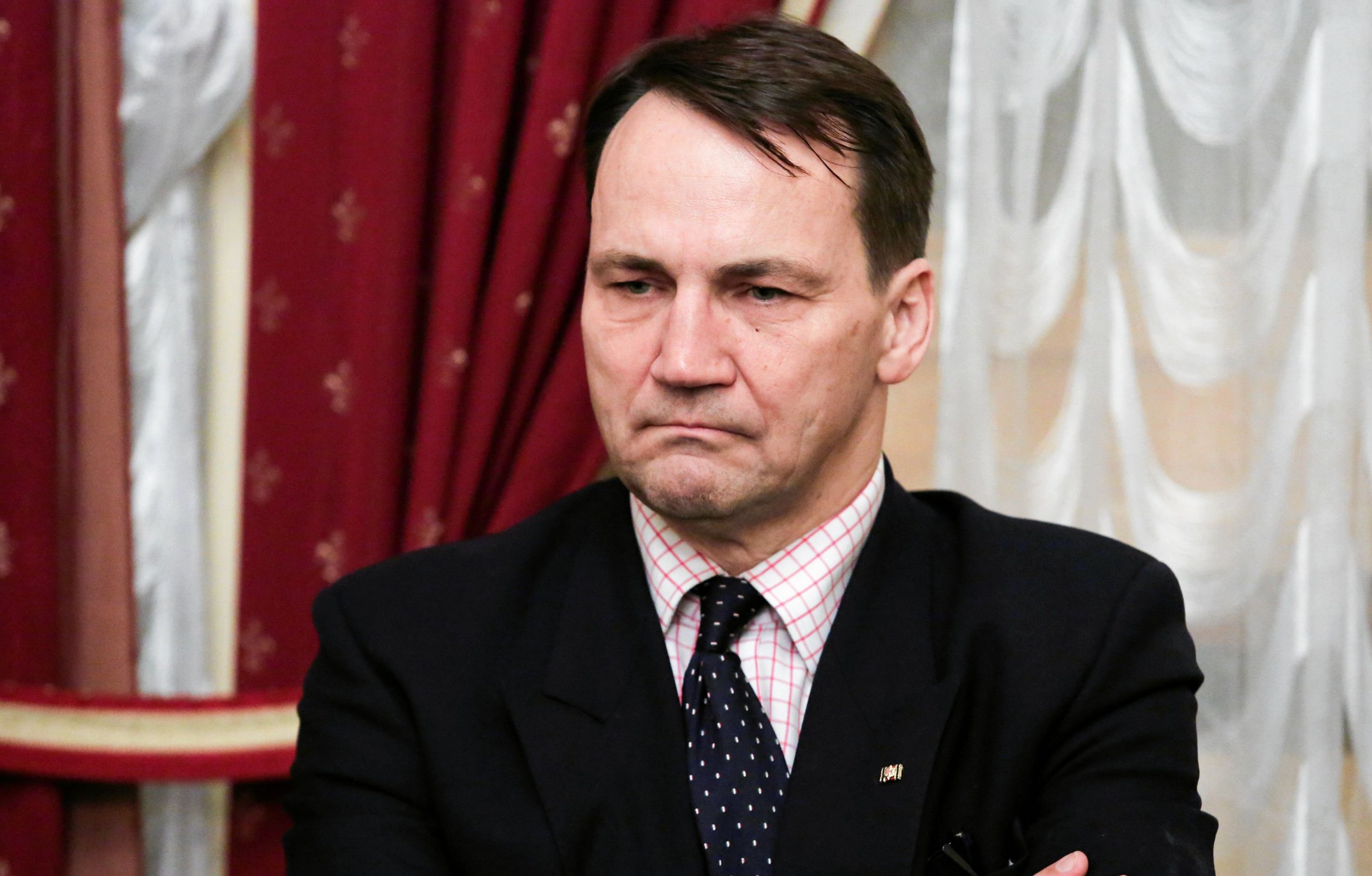 Radosław Sikorski stoi z nietęgą miną ze skrzyżowanymi rękami
