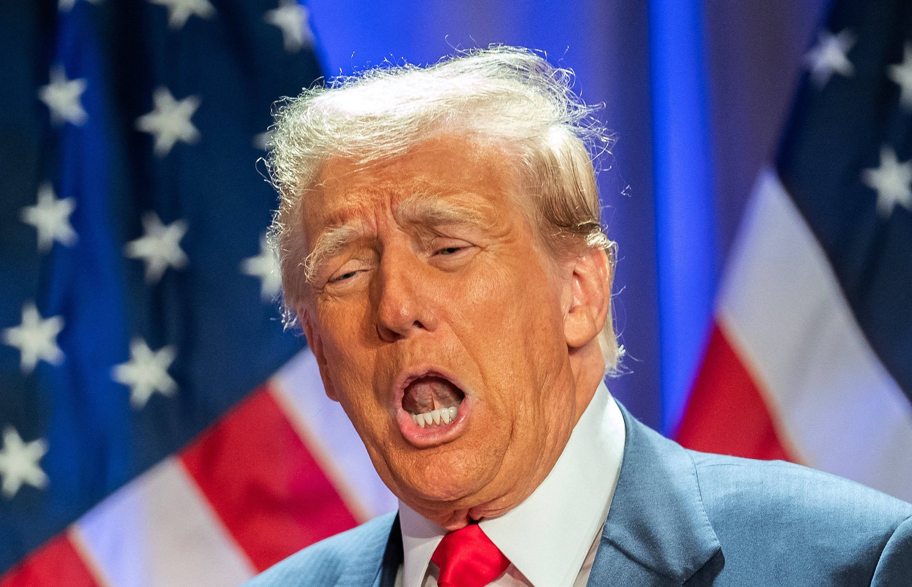 Donald Trump z otwartymi ustami i dziwną miną. W tle flagi USA