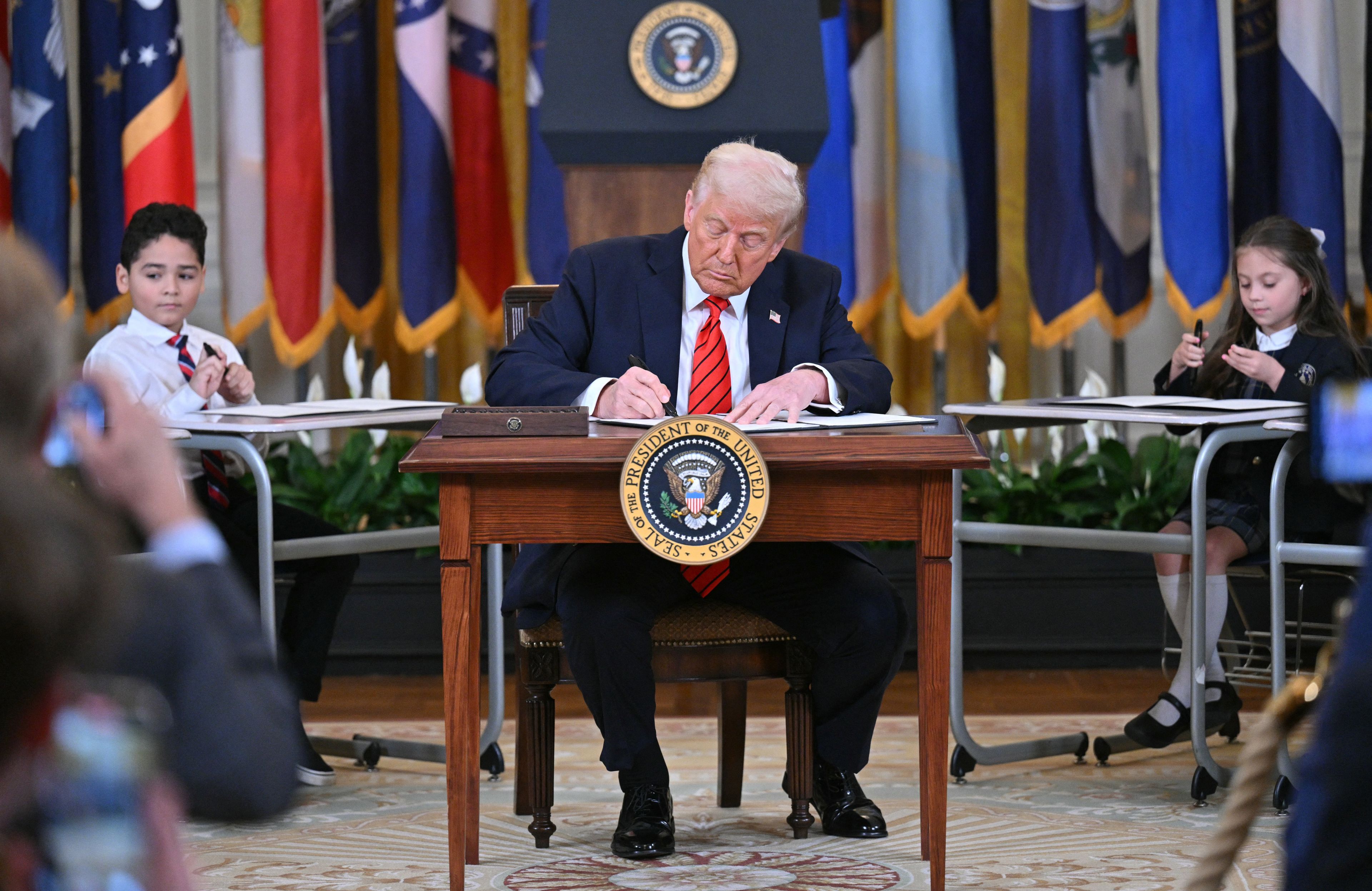 Prezydent USA Donald Trump podpisuje rozporządzenie siedzac w ławce szkolnej