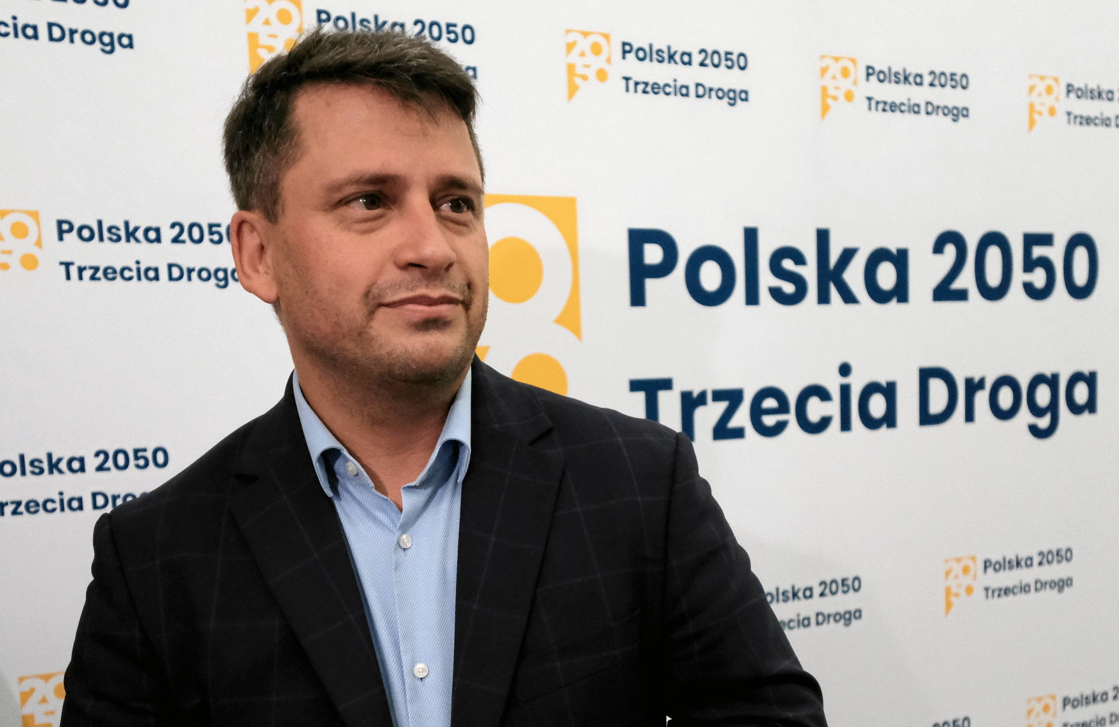 Paweł Śliz pozuje na tle białej ścianki z żółtymi napisami "Polska 2050. Trzecia Droga"