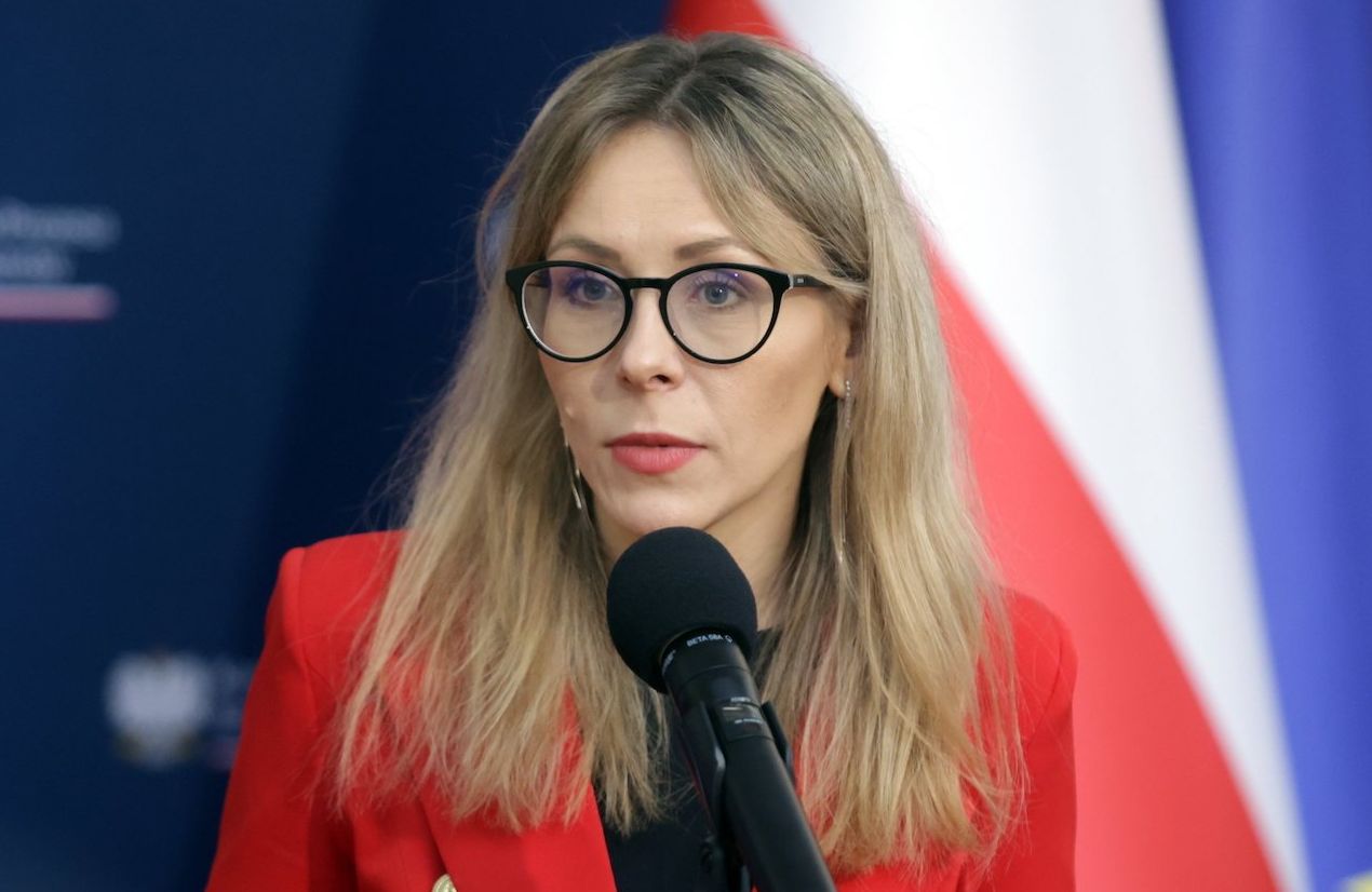Agnieszka Buczyńska w czerwonej marynarce i ciemnej koszuli. Długowłosa blondynka w ciemnych oprawkach.