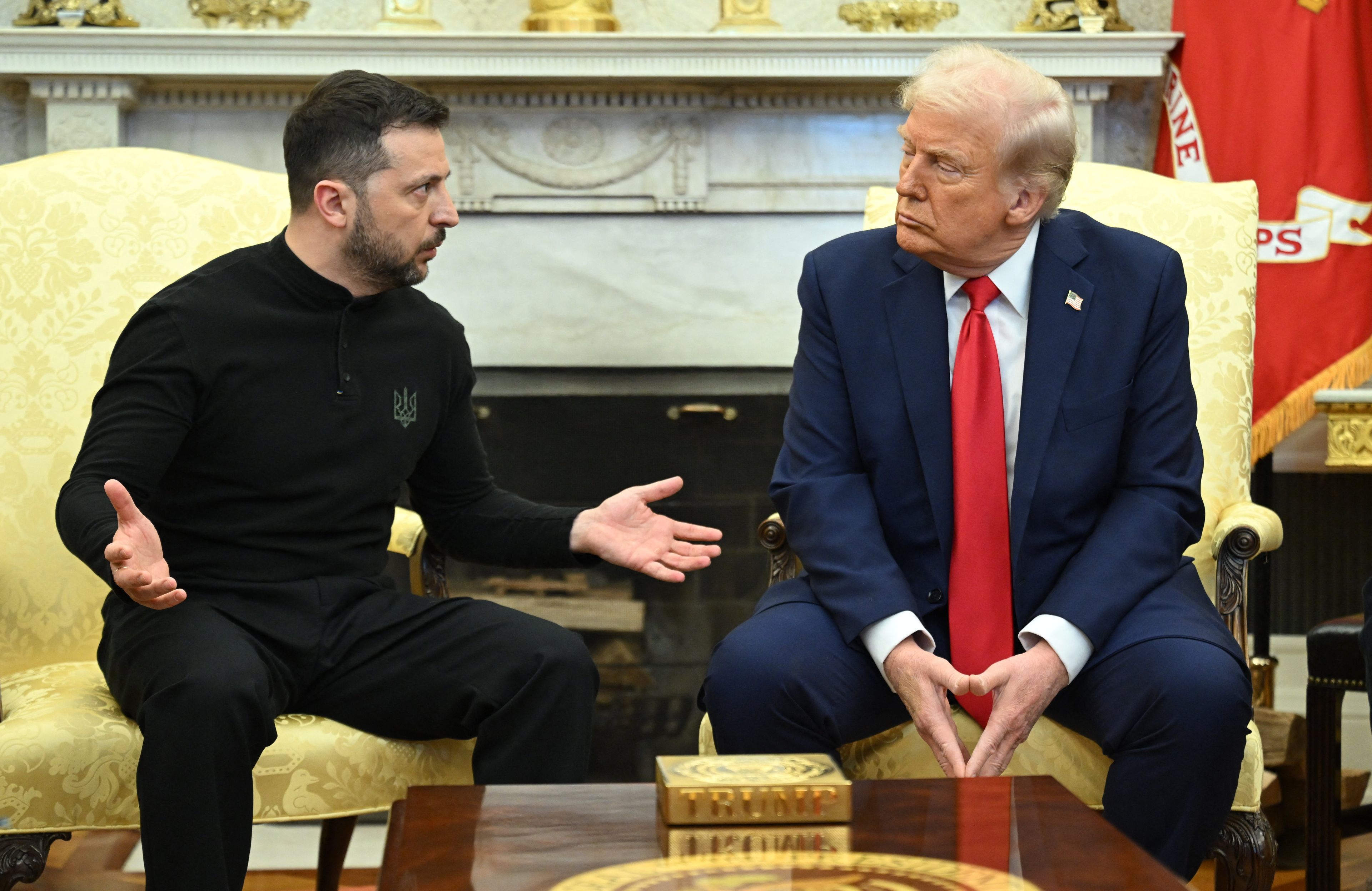 Wołodymyr Zełenski rozkłada ręce, Donald Trump patrzy na niego wrogo. W tle kominek