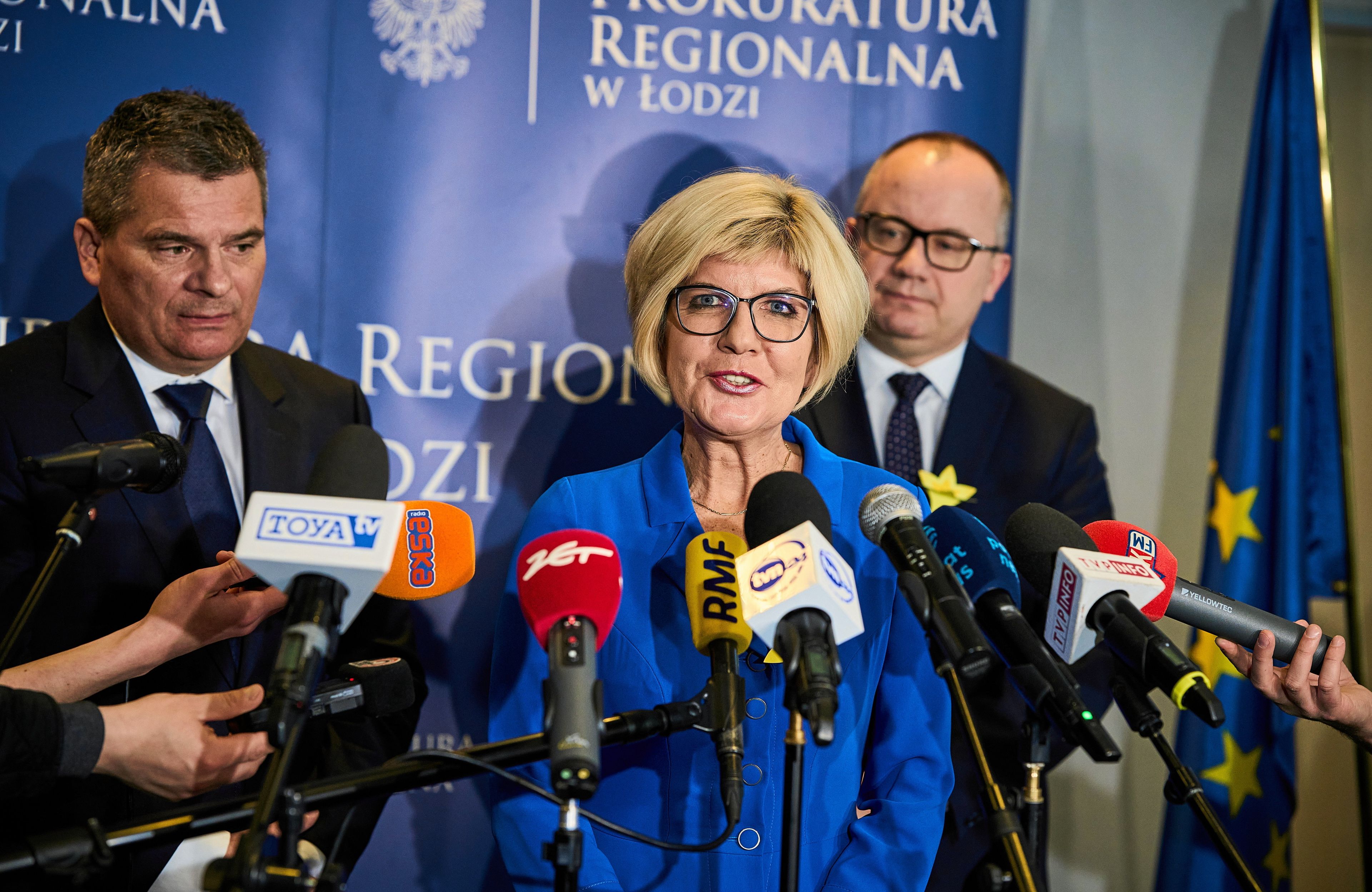Trzy osoby na konferencji prasowej,, w środku kobieta