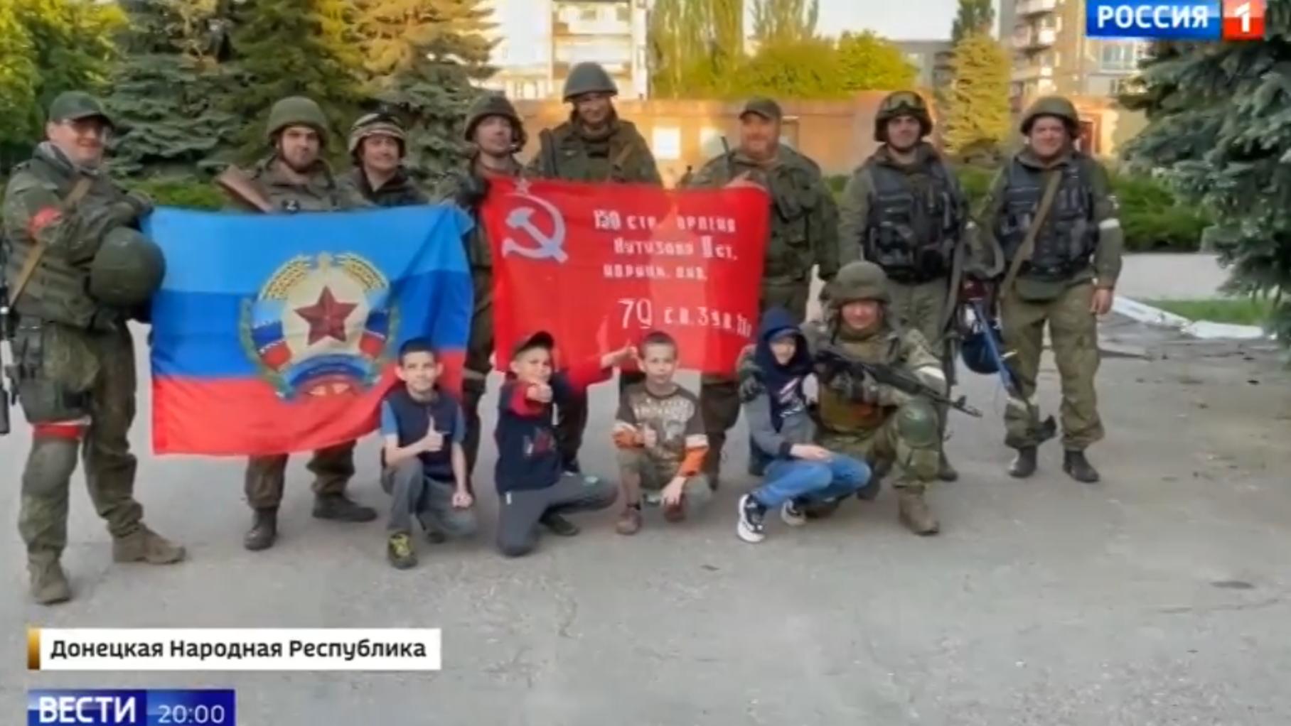 Dzieci i żołnierze pozują do zbiorowej fotografii na tle sowieckiej flagi