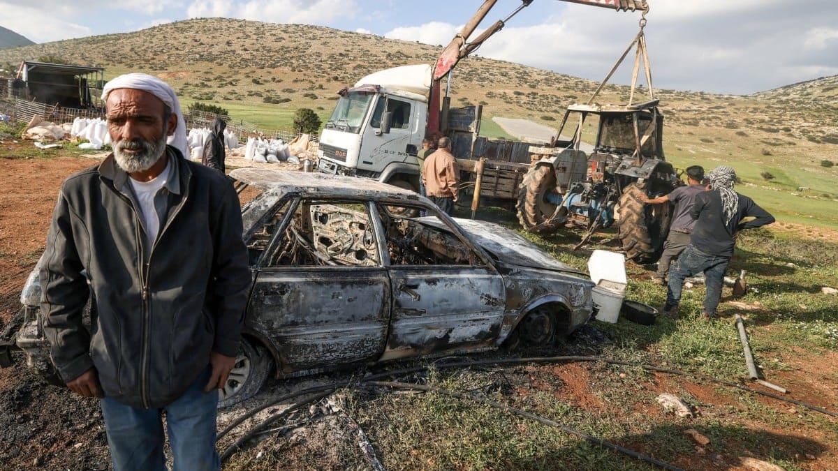 Starszy mężczyzna na tle spalonego samochodu po ataku osadników na Zachodnim Brzegu