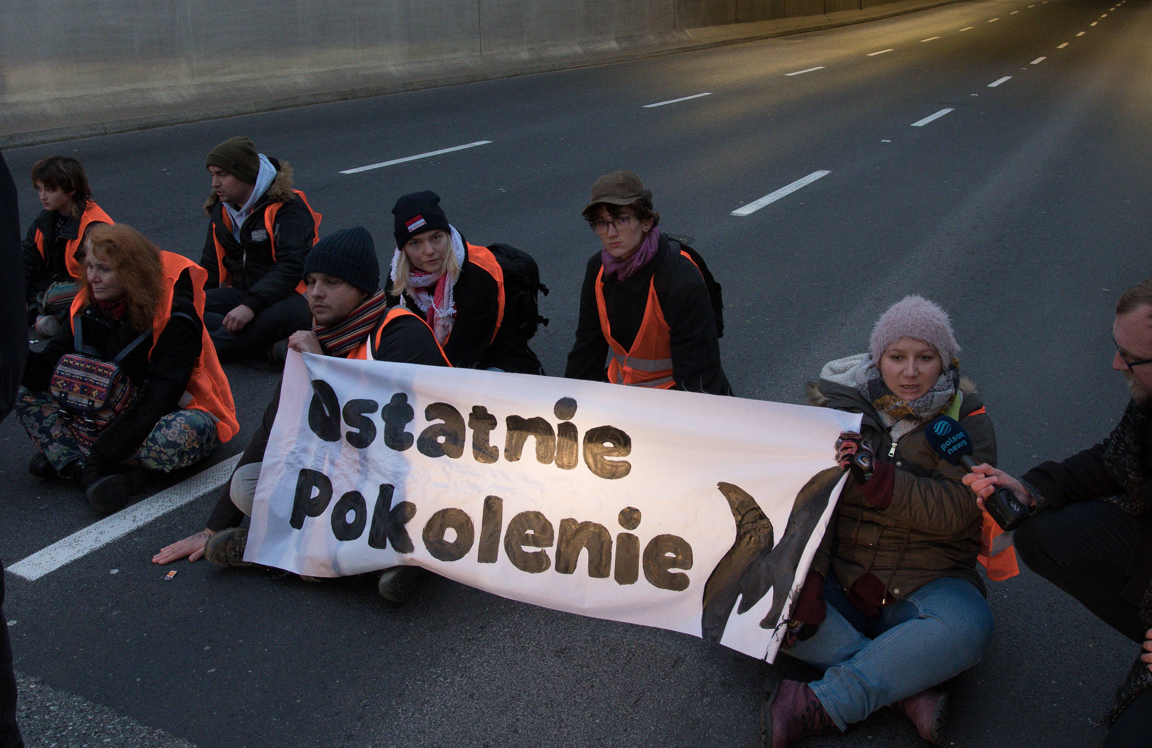 aktywiści z napisem ostatnie pokolenie siedzą na drodze