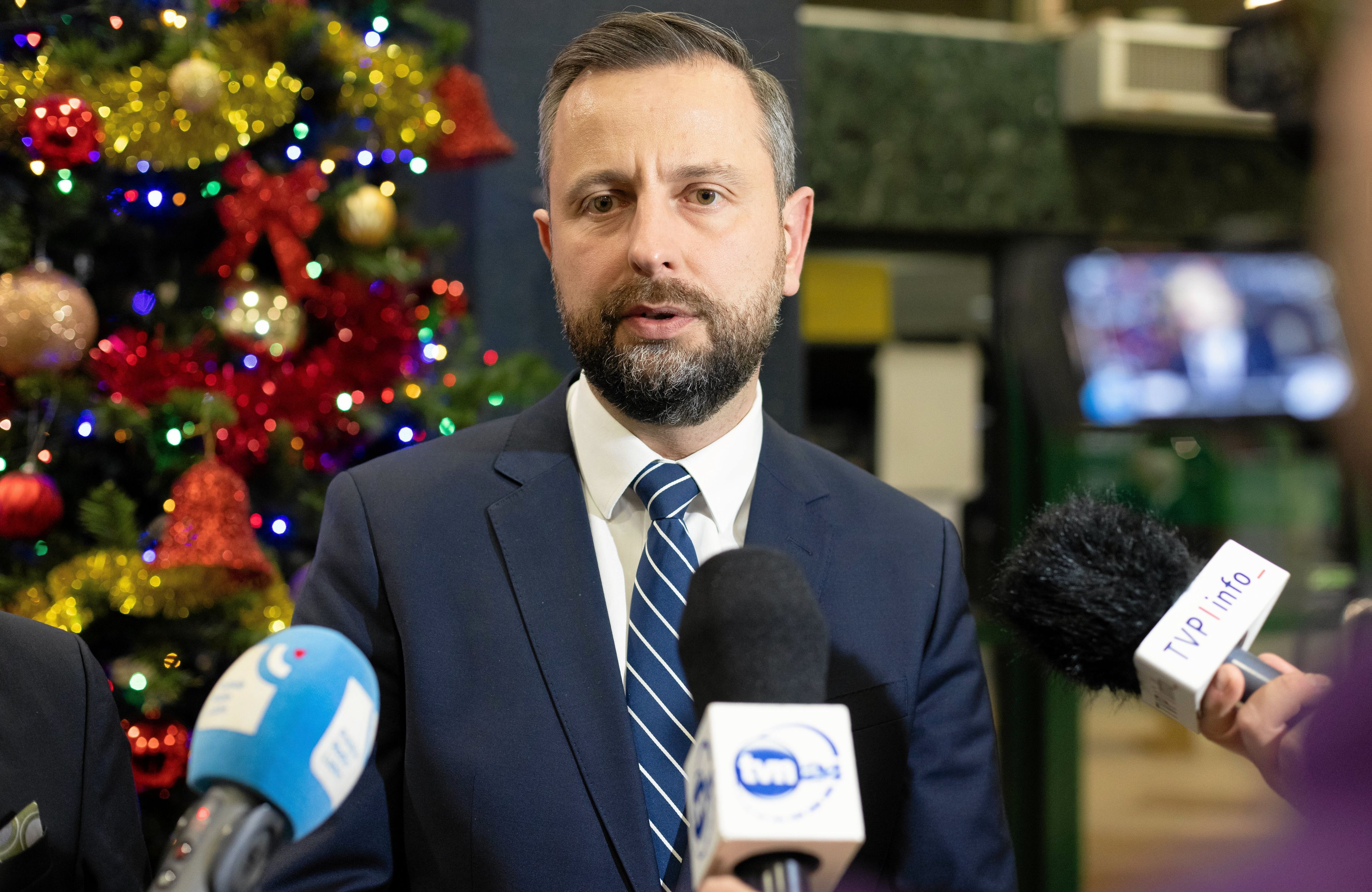 Władysław Kosiniak Kamysz odpowiada na tle choinki na pytania dziennikarzy. Przed nim stoją mikrofony różnych stacji