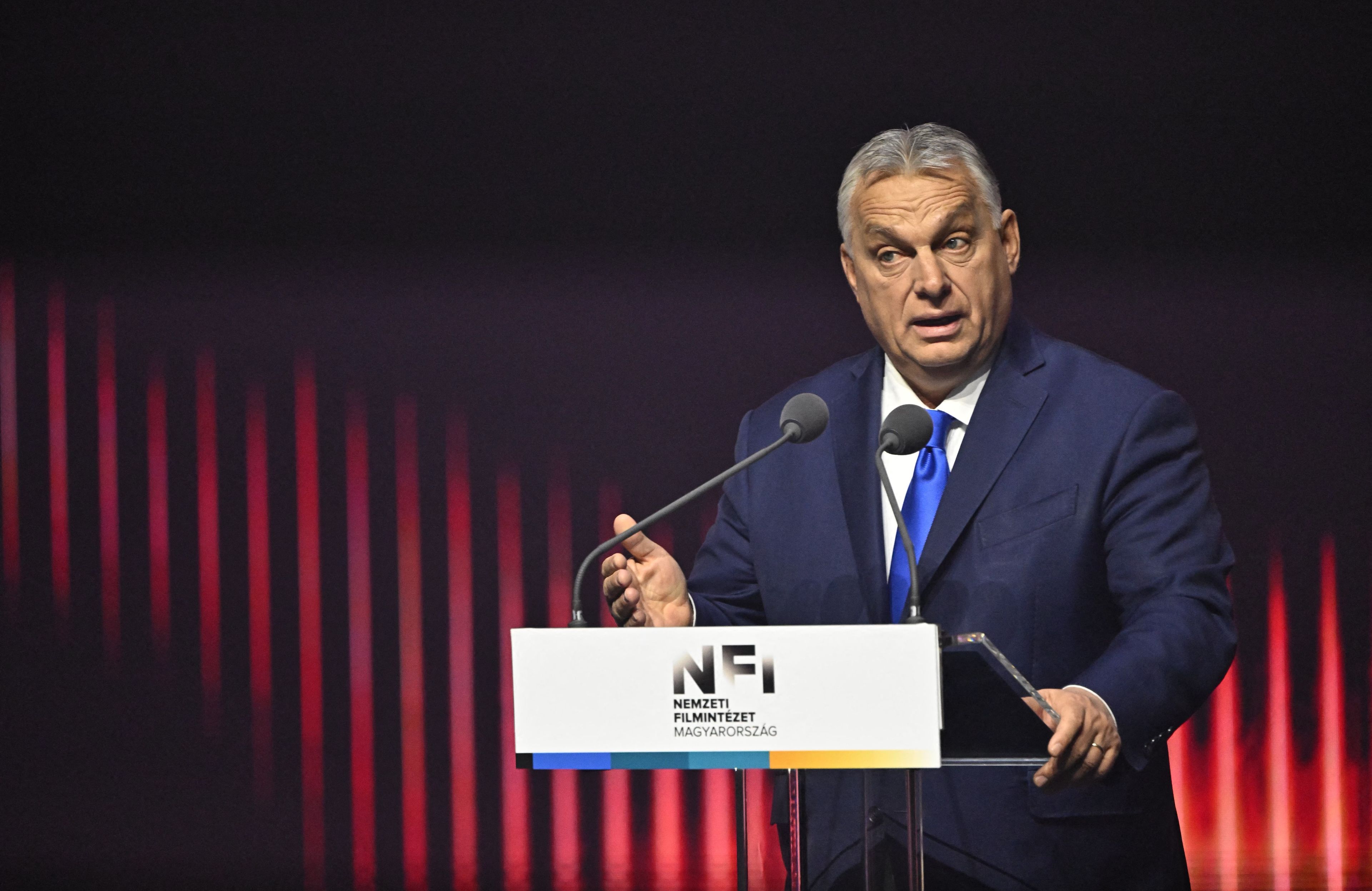 Premier Węgier przemawia do mikrofonu na czerwonym tle