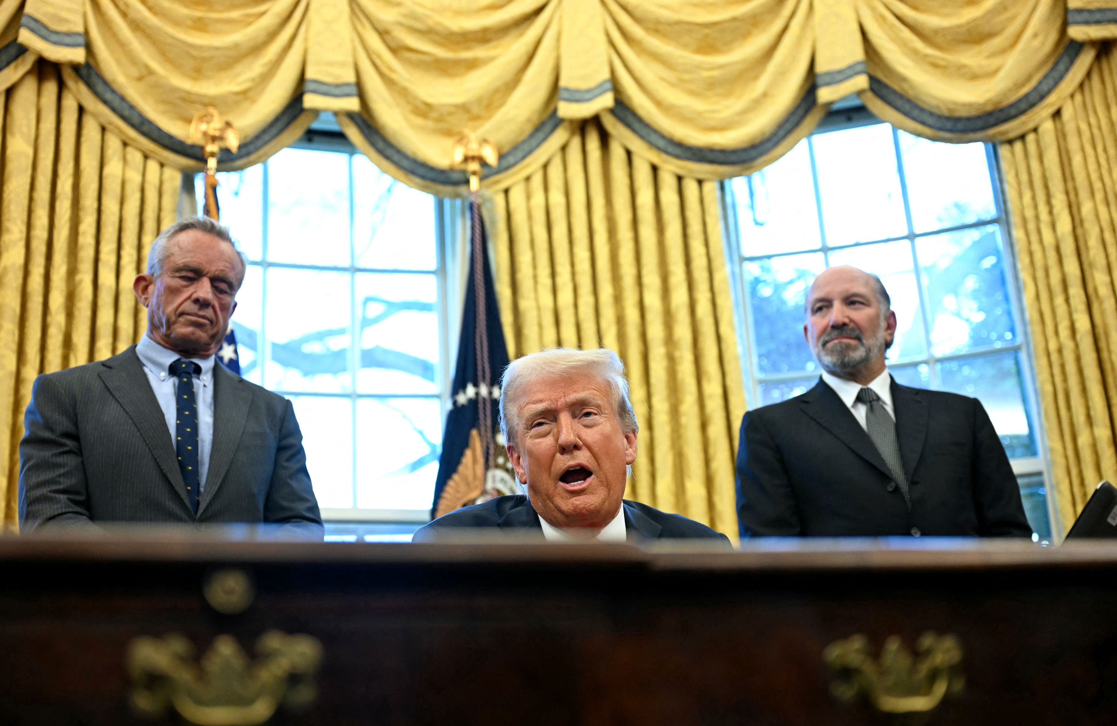 Donald Trump przemawia za biurkiem w Gabinecie Owalnym, w tle złote zasłony