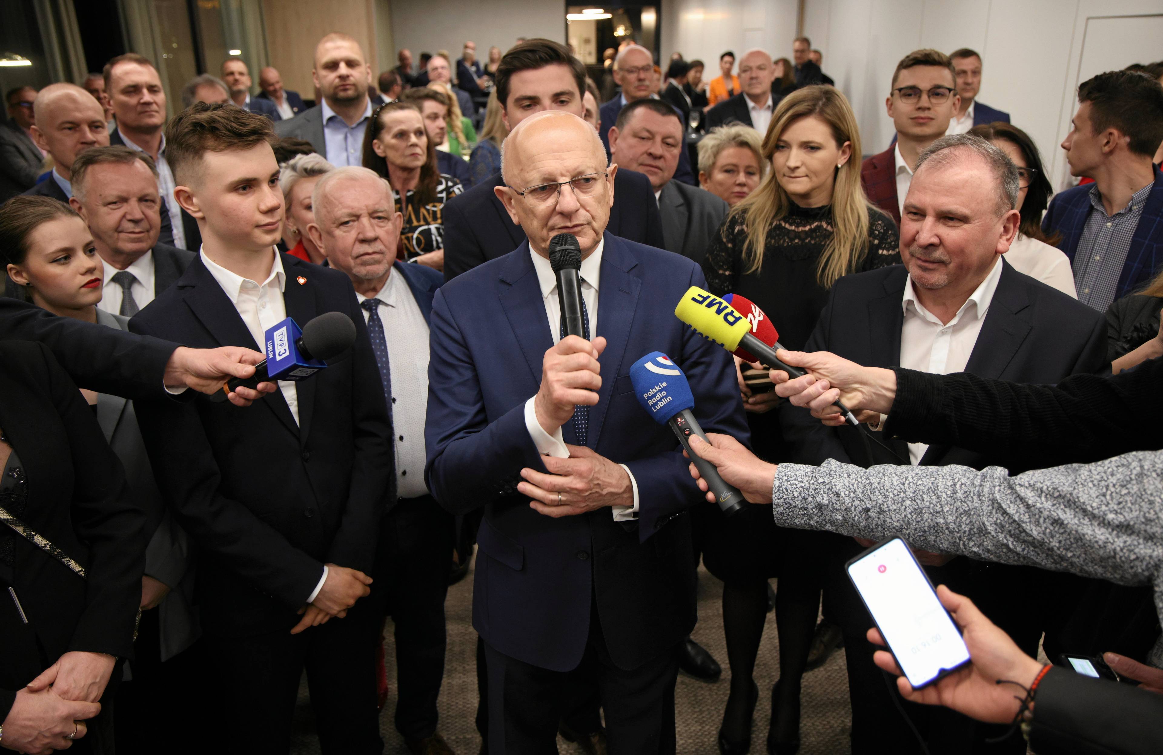 Mężczyzna w otoczeniu grupy osób odpowiada na pytania dziennikarzy. Województwo lubelskie - wybory