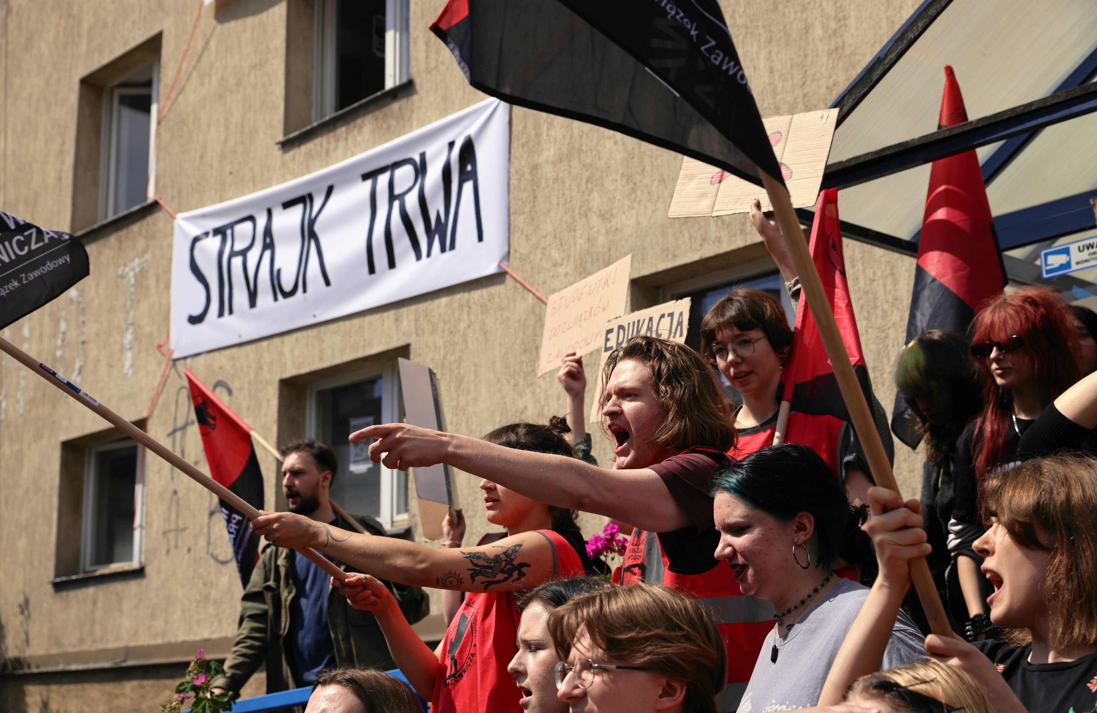 Protestujący przed budynkiem akademika Kamionka w Krakowie machają flagami, w tle napis "strajk trwa"