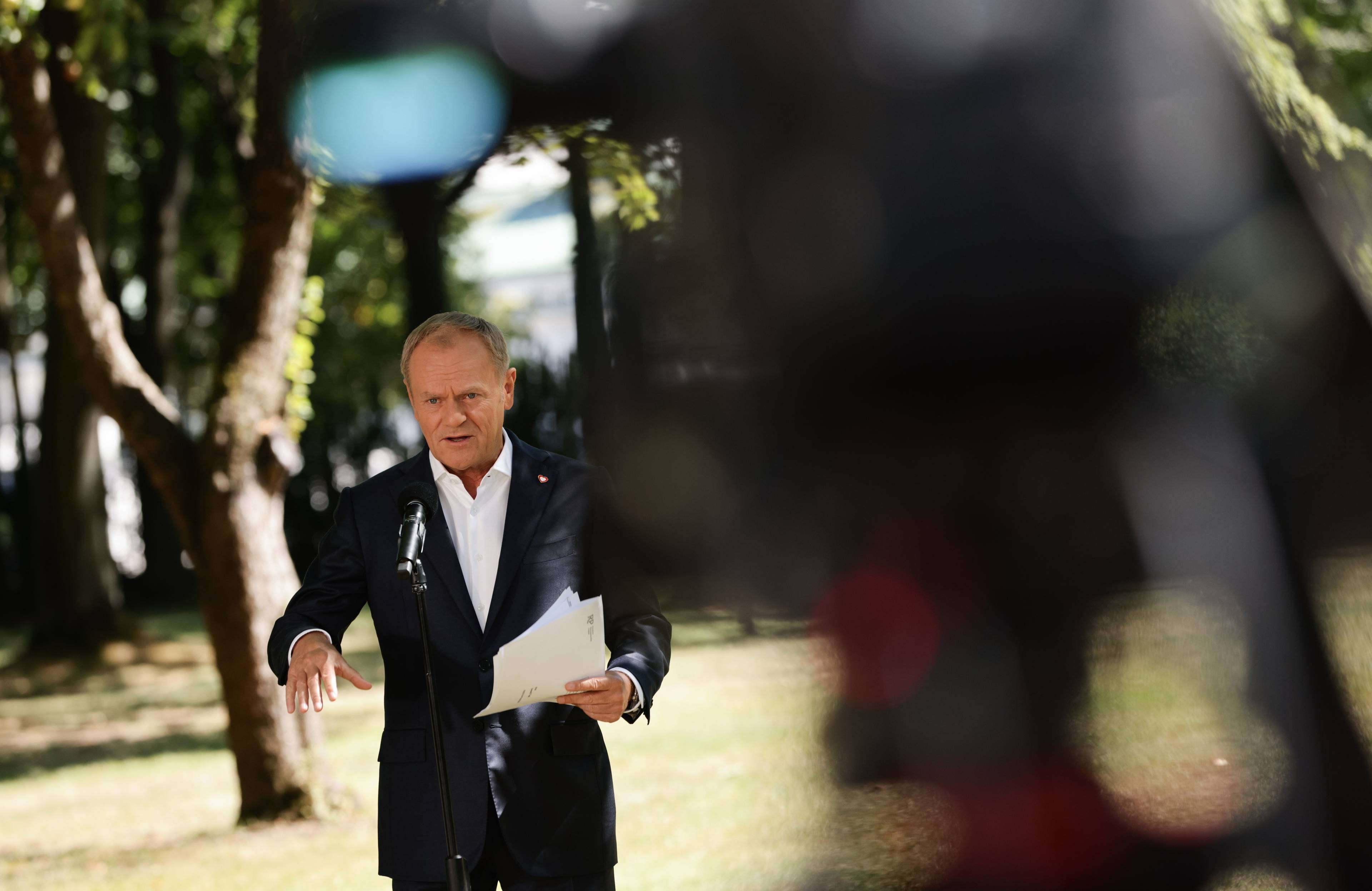 Donald Tusk nówi do mikrofonu na tle parku