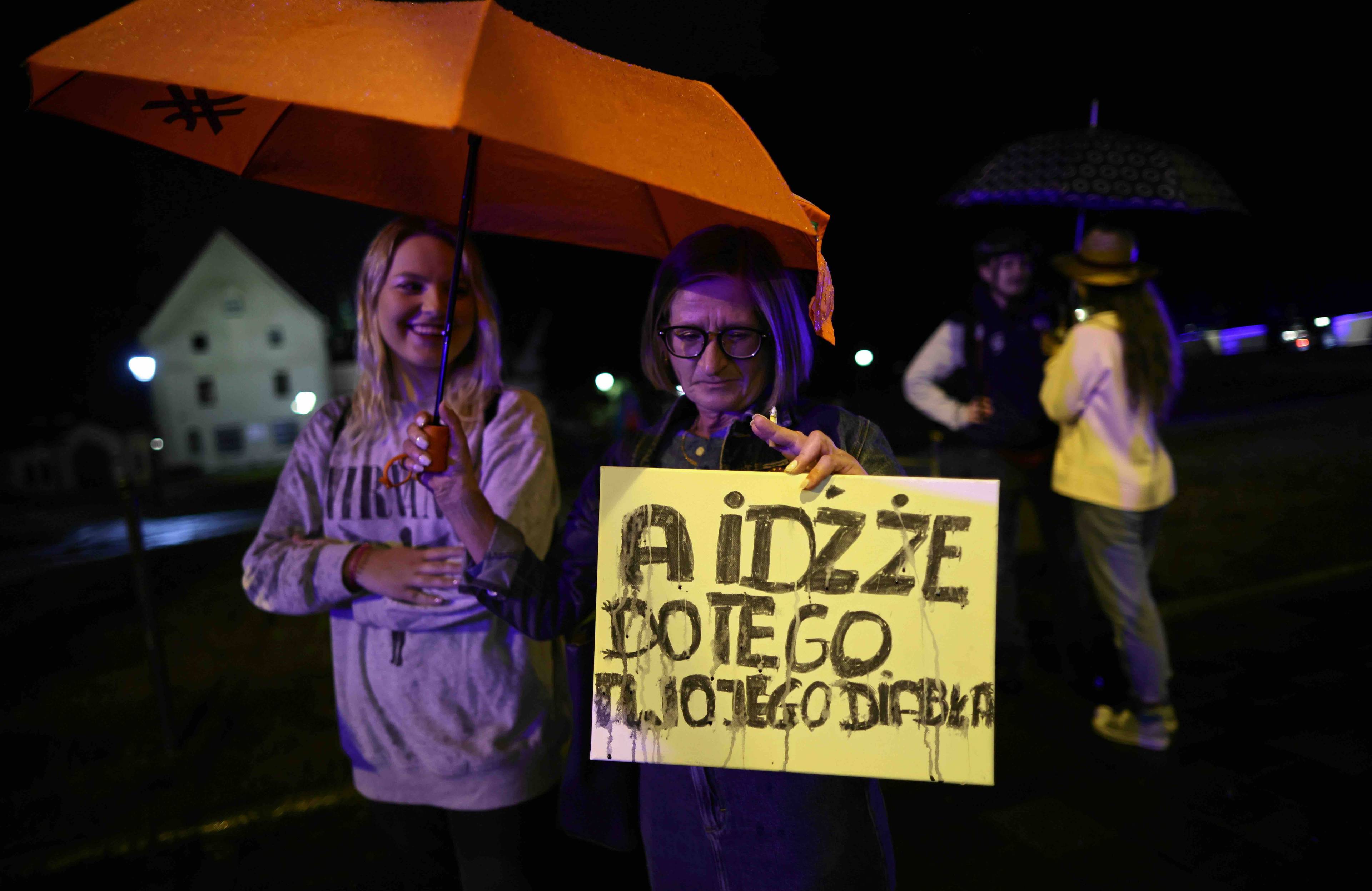 Kobieta i mężczyzna stoją przed siedzibą kurii w Krakowie trzymając plakat z napisem {A idźże do tego twojego diabła”. Abp Jędraszewski