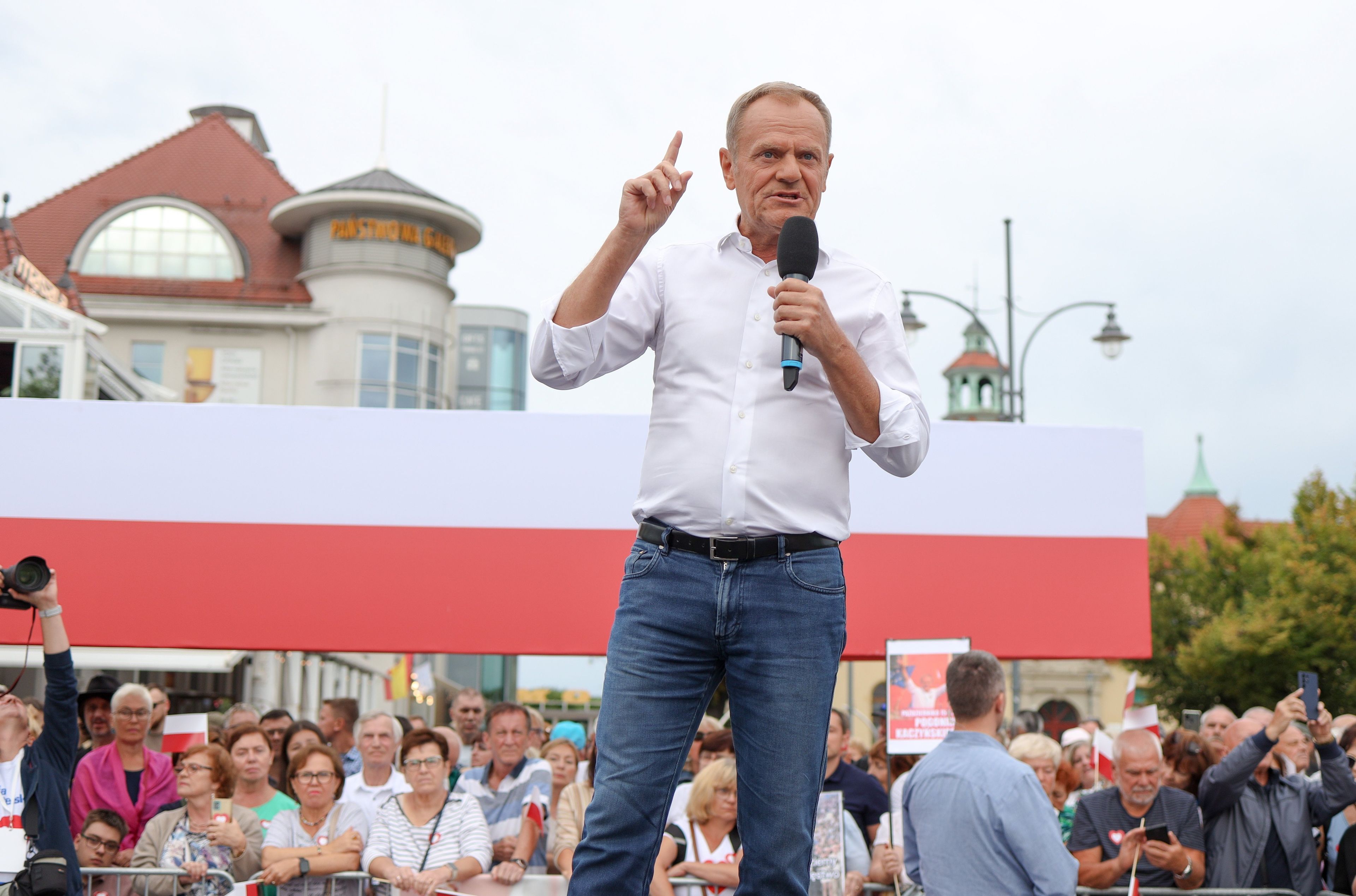 Donald Tusk w białej koszuli z mikrofonem w ręku przemawia do tłumu ludzi