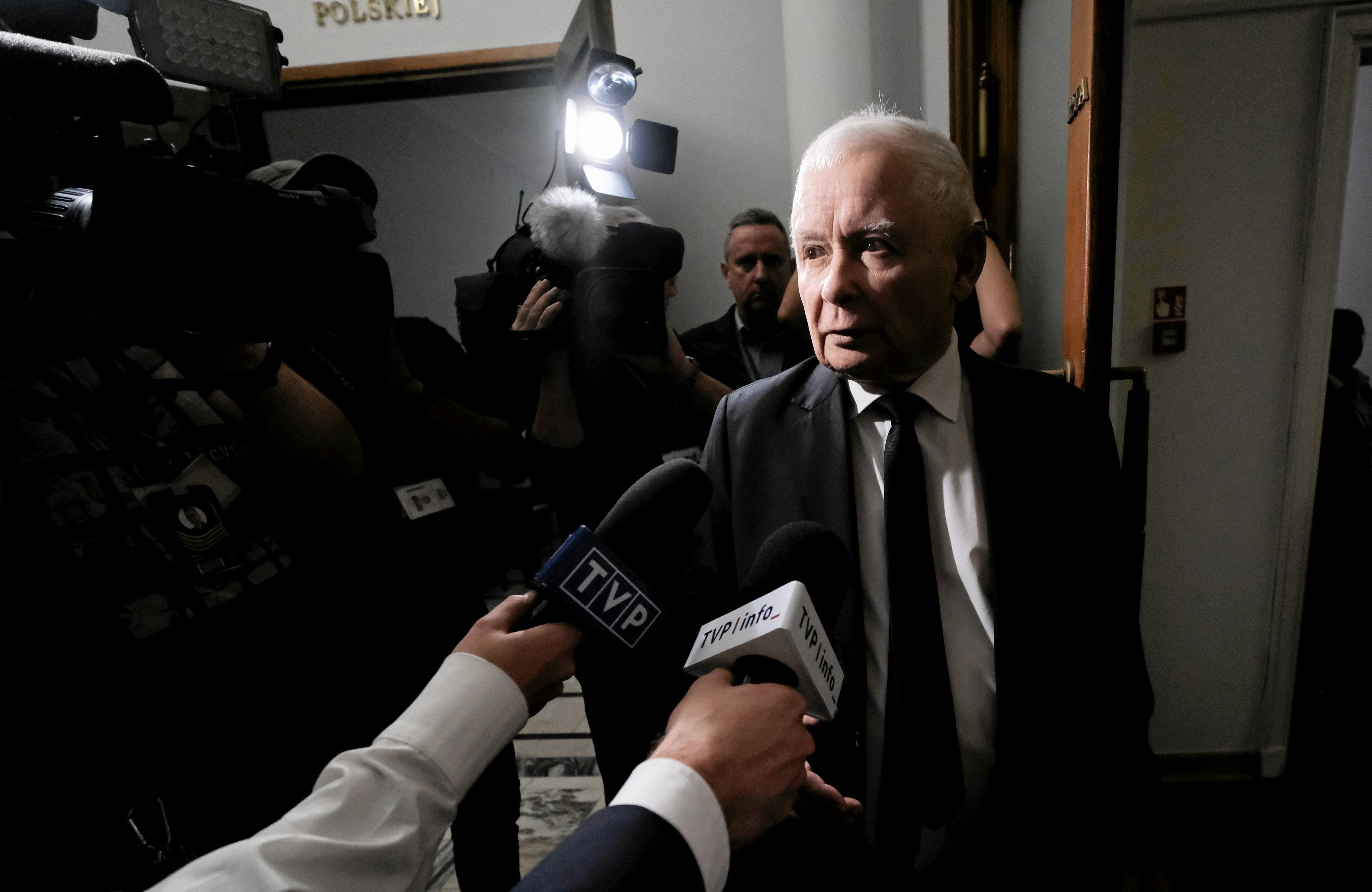 Prezes PiS oświetlony światłem z kamer stoi przed mikrofonami dziennikarzy