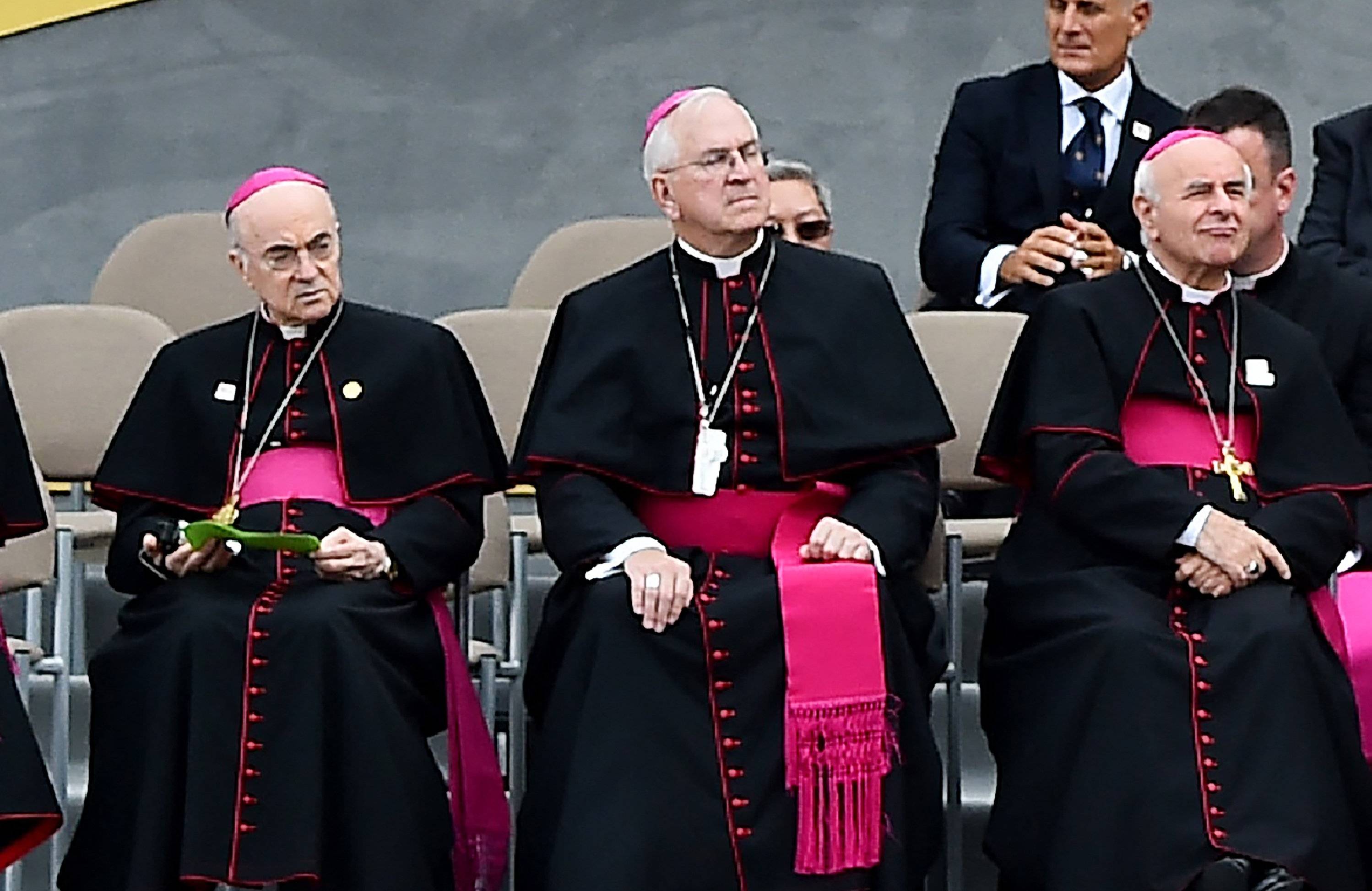Trzech siedzących biskupów w czarnych sutannach z purpurowymi pasami. Z lewej – abp Viganò