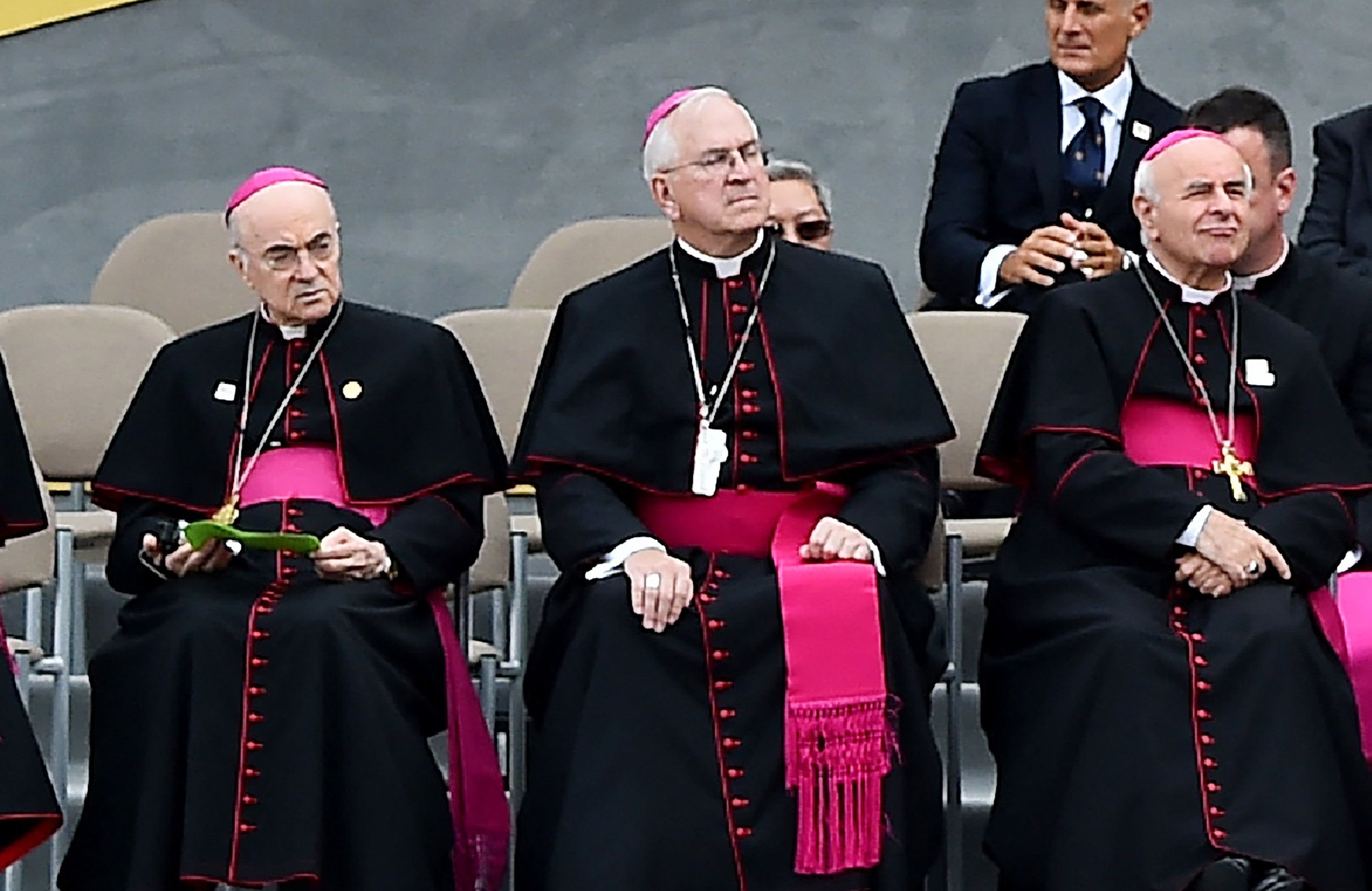 Trzech siedzących biskupów w czarnych sutannach z purpurowymi pasami. Z lewej – abp Viganò