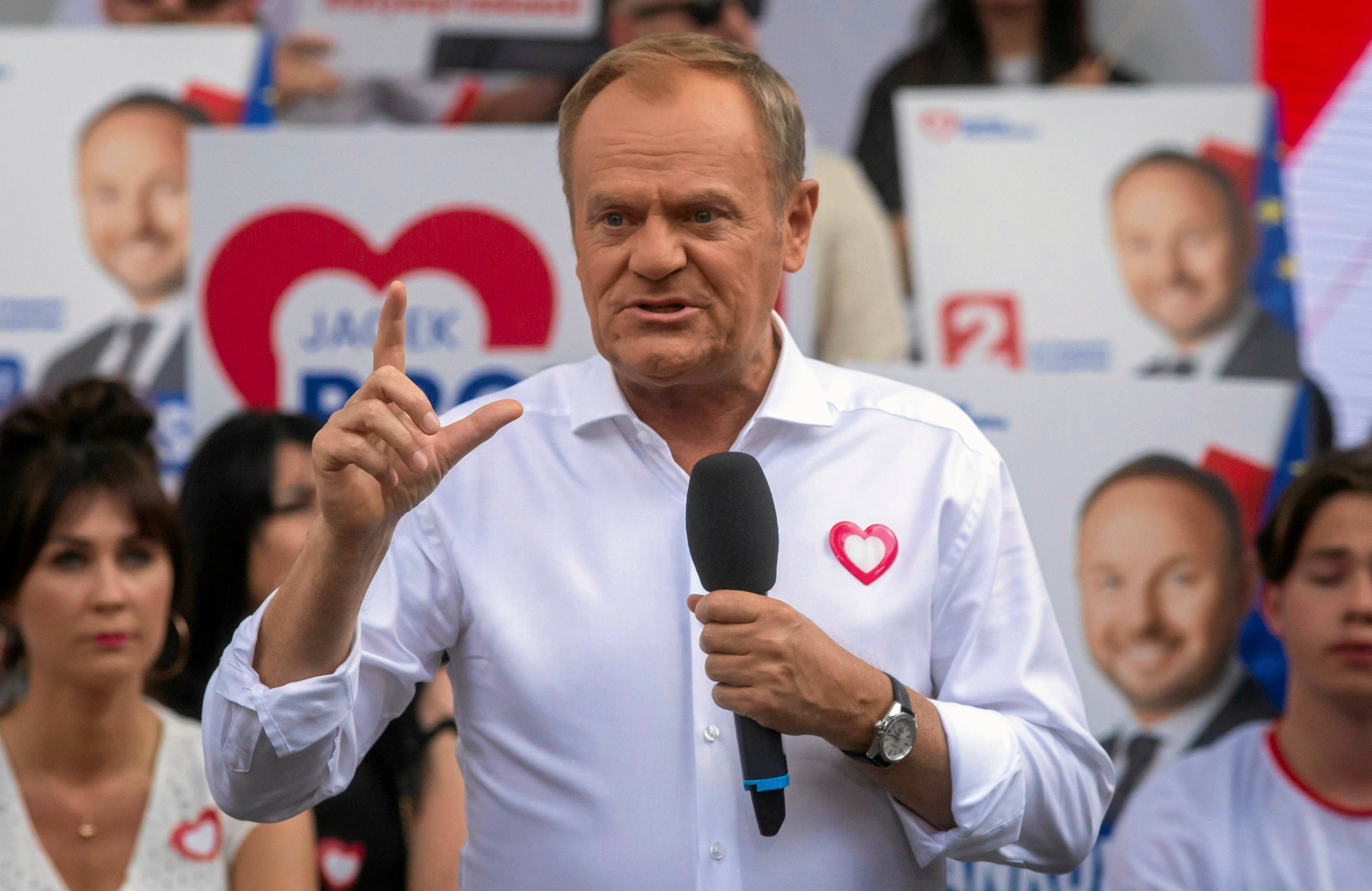 Donald Tusk przemawia w białej koszuli z symbolem biało-czerwonego serca