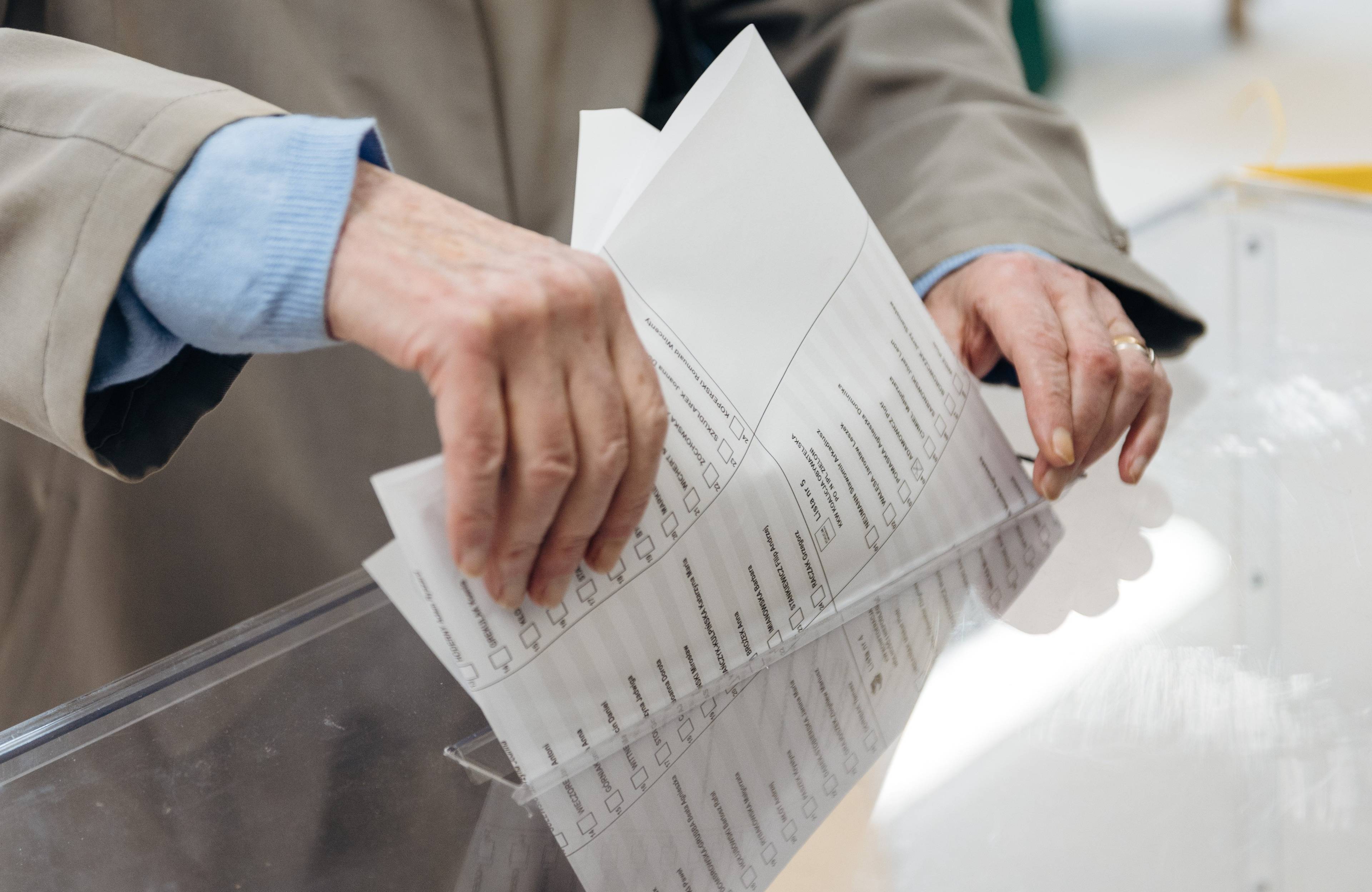 Dłoń wrzuca kartkę do urny wyborczej