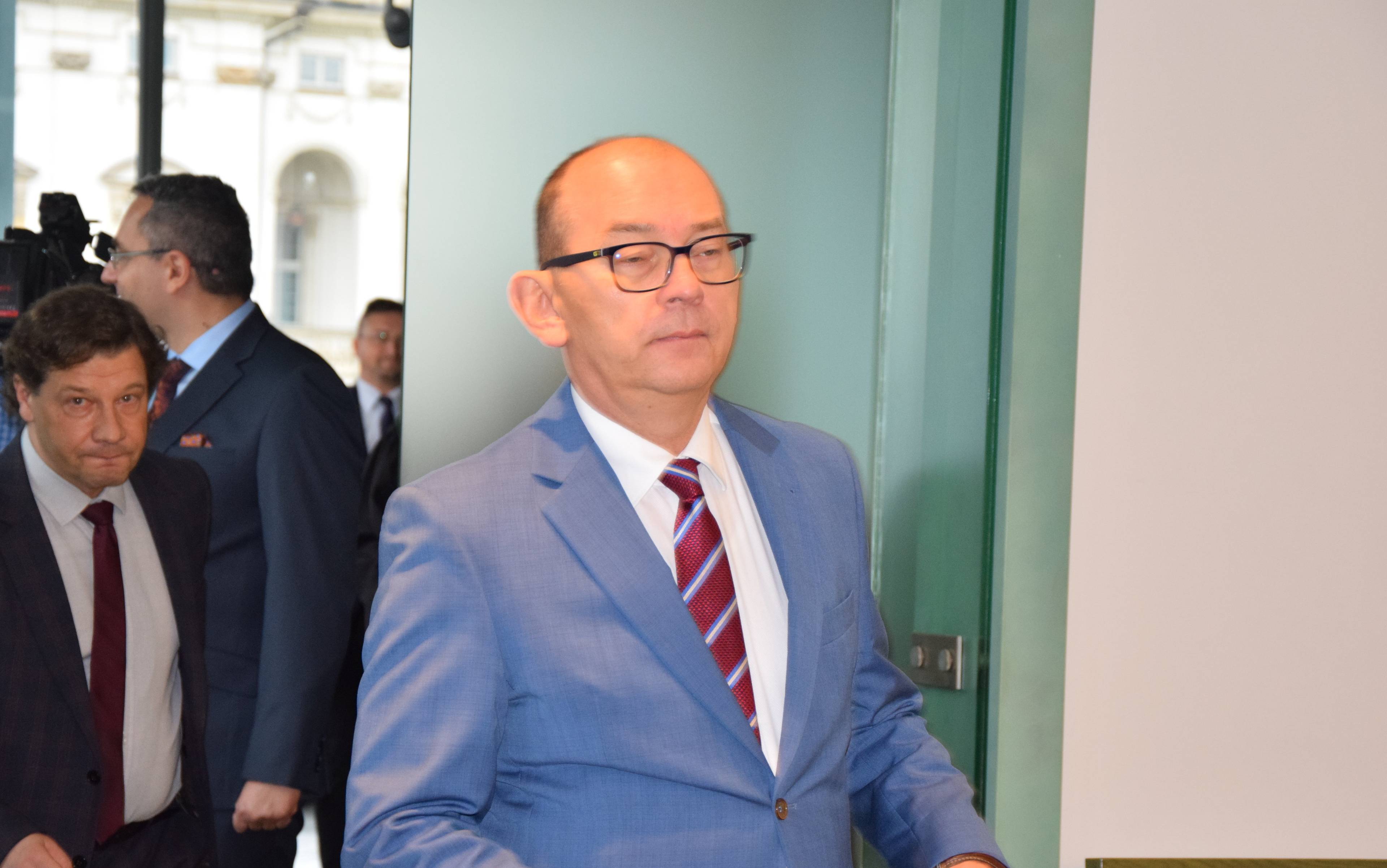 Na zdjęciu Przemysław Radzik, łysy mężczyzna w okularach i jasnoniebieskim garniturze na korytarzu sądowym