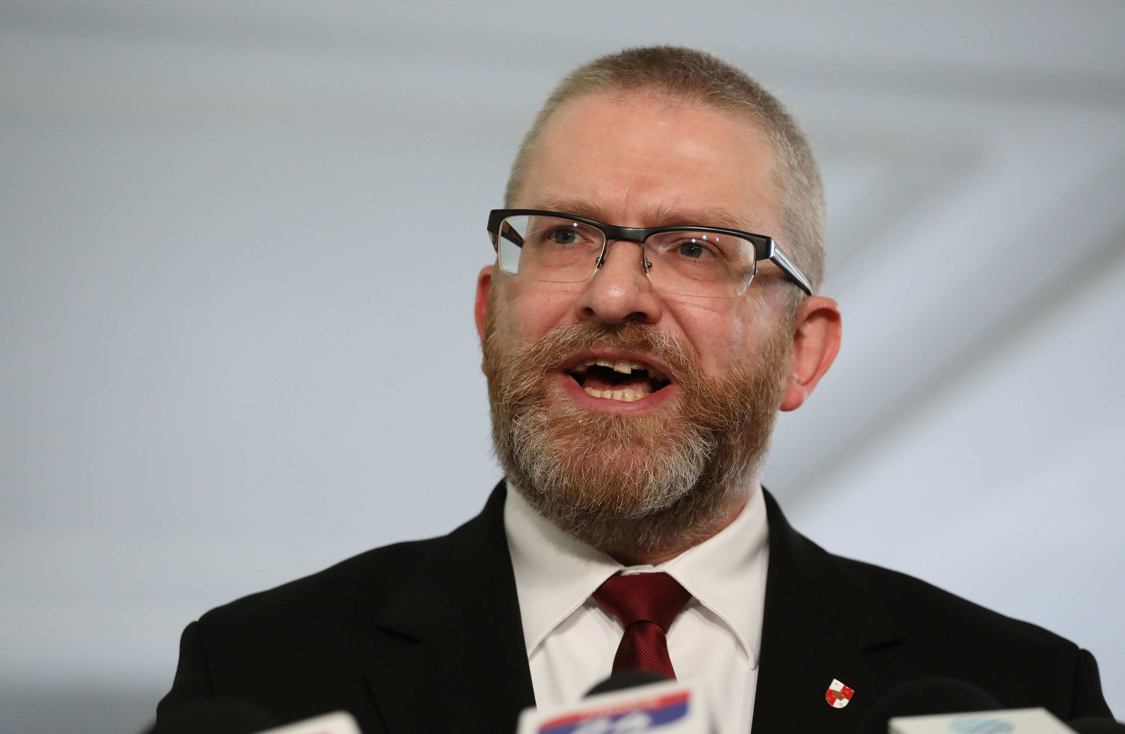 Męzczyzna w garniturze, z brodą i w okularach (poseł Konfederacji Grzegorz Braun), który przemawia do dziennikarzy
