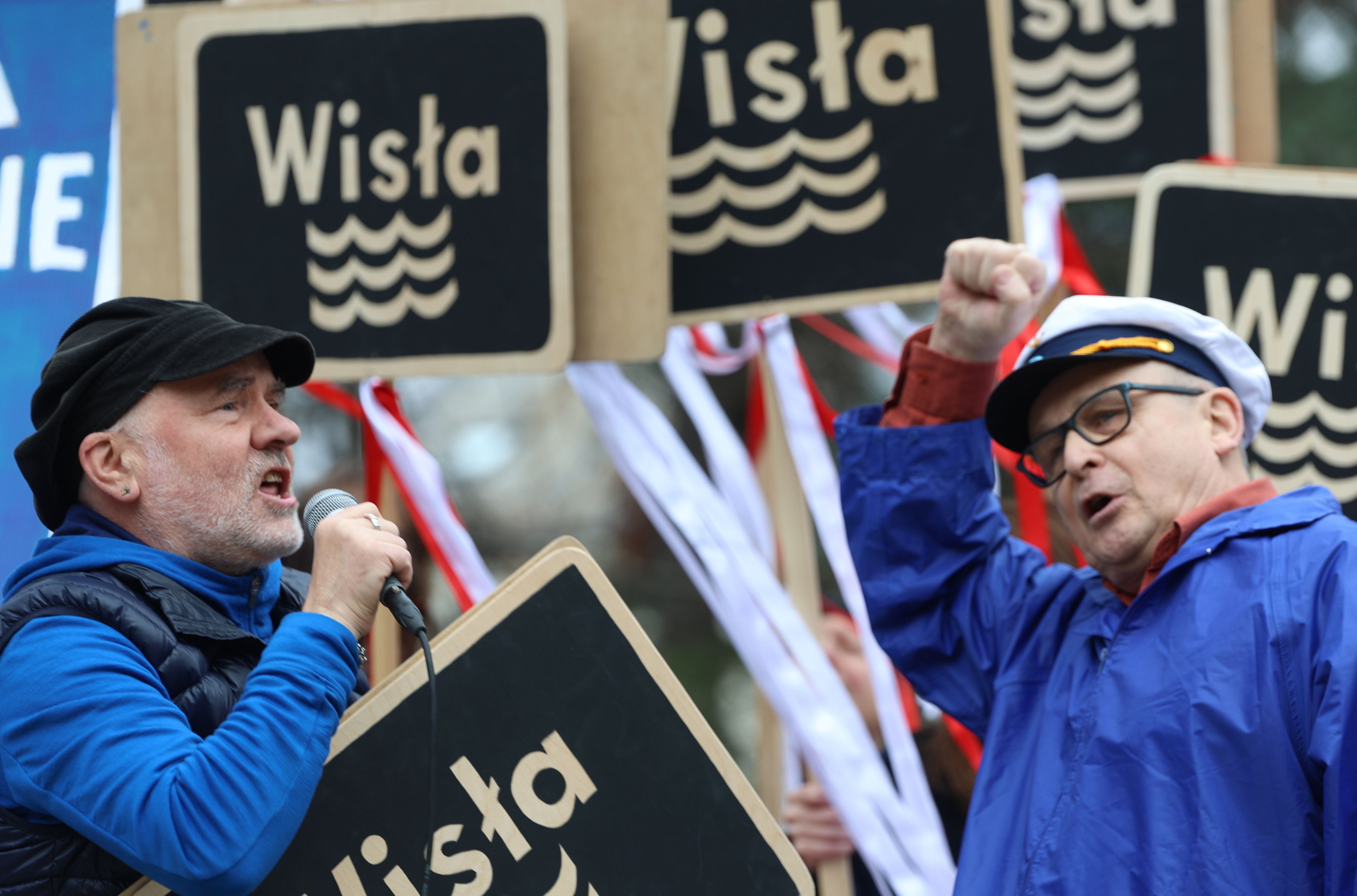 Dwóch mężczyzn przemawia na proteście, a za ich plecami widać tabliczki z napisem Wisła