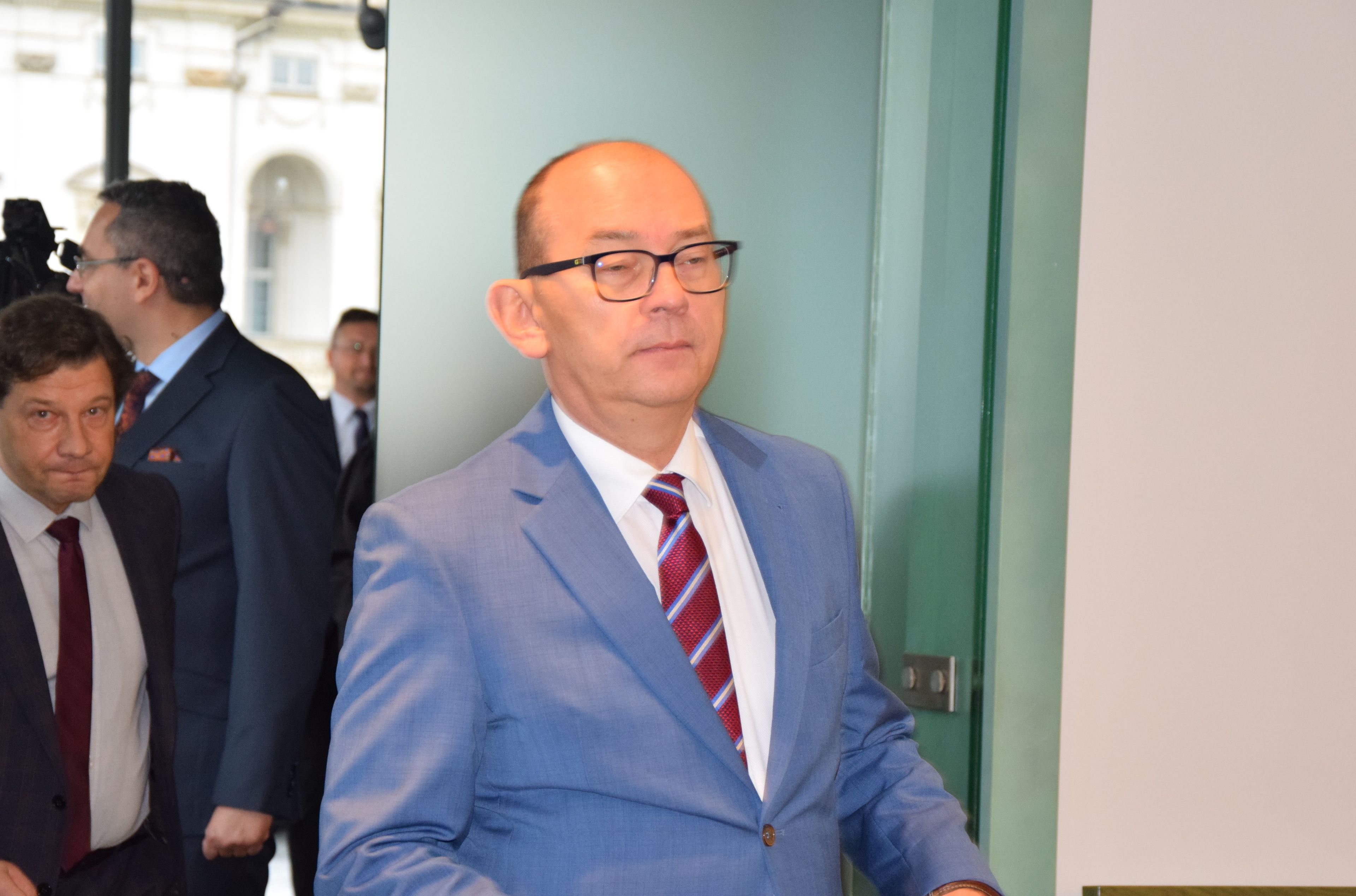 Na zdjęciu Przemysław Radzik, łysy mężczyzna w okularach i jasnoniebieskim garniturze na korytarzu sądowym