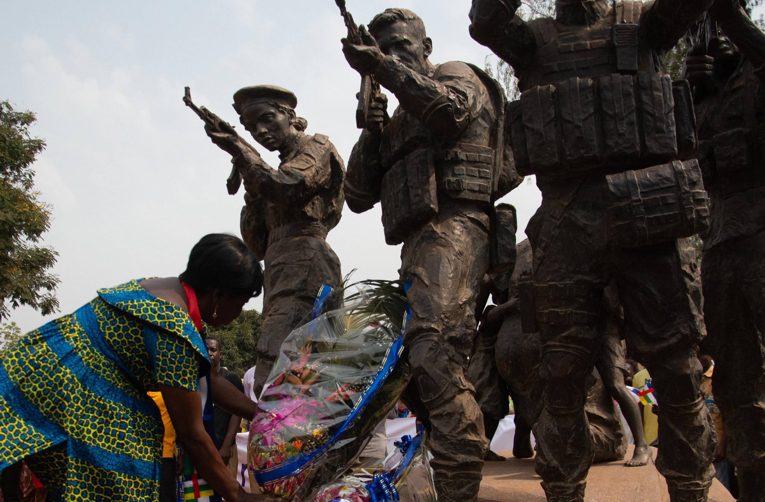 Afrykanka w barwnej sukni składa kwiaty pod pomnikiem przedstawiającym żołnierzy