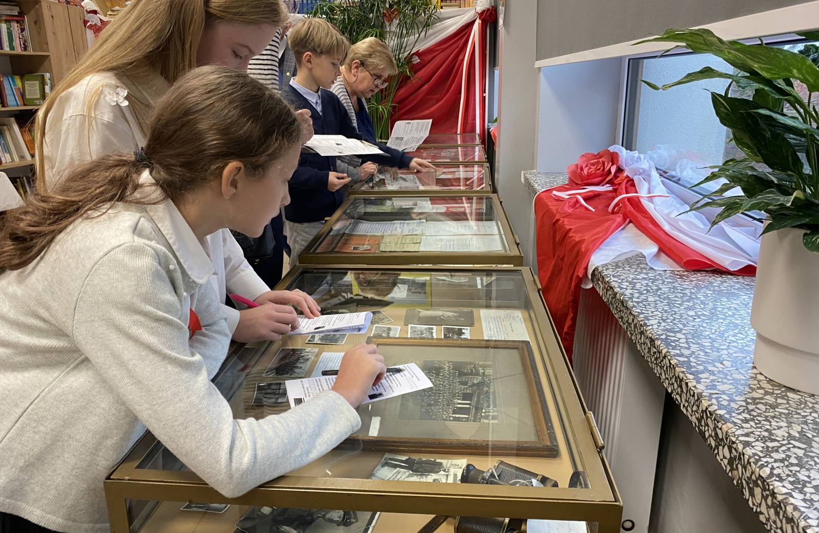 Dwie dziewczynki pochylają sie nad gablotą w bibliotece i rozwiązują zadanie