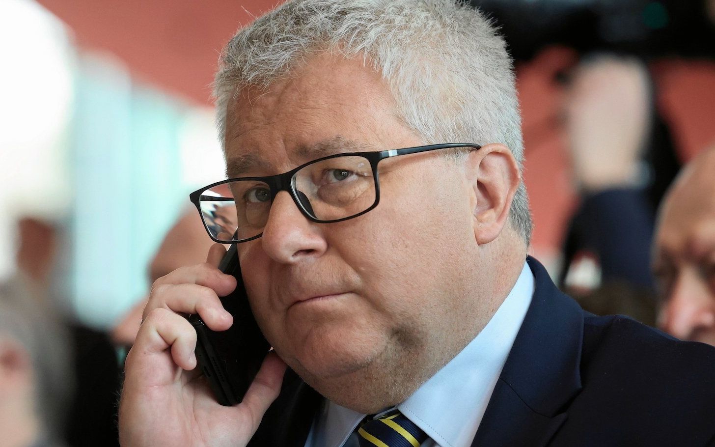 Ryszard Czarnecki w ciemnej marynarce i krawacie w granatowo-żółte paski rozmawia przez telefon komórkowy.