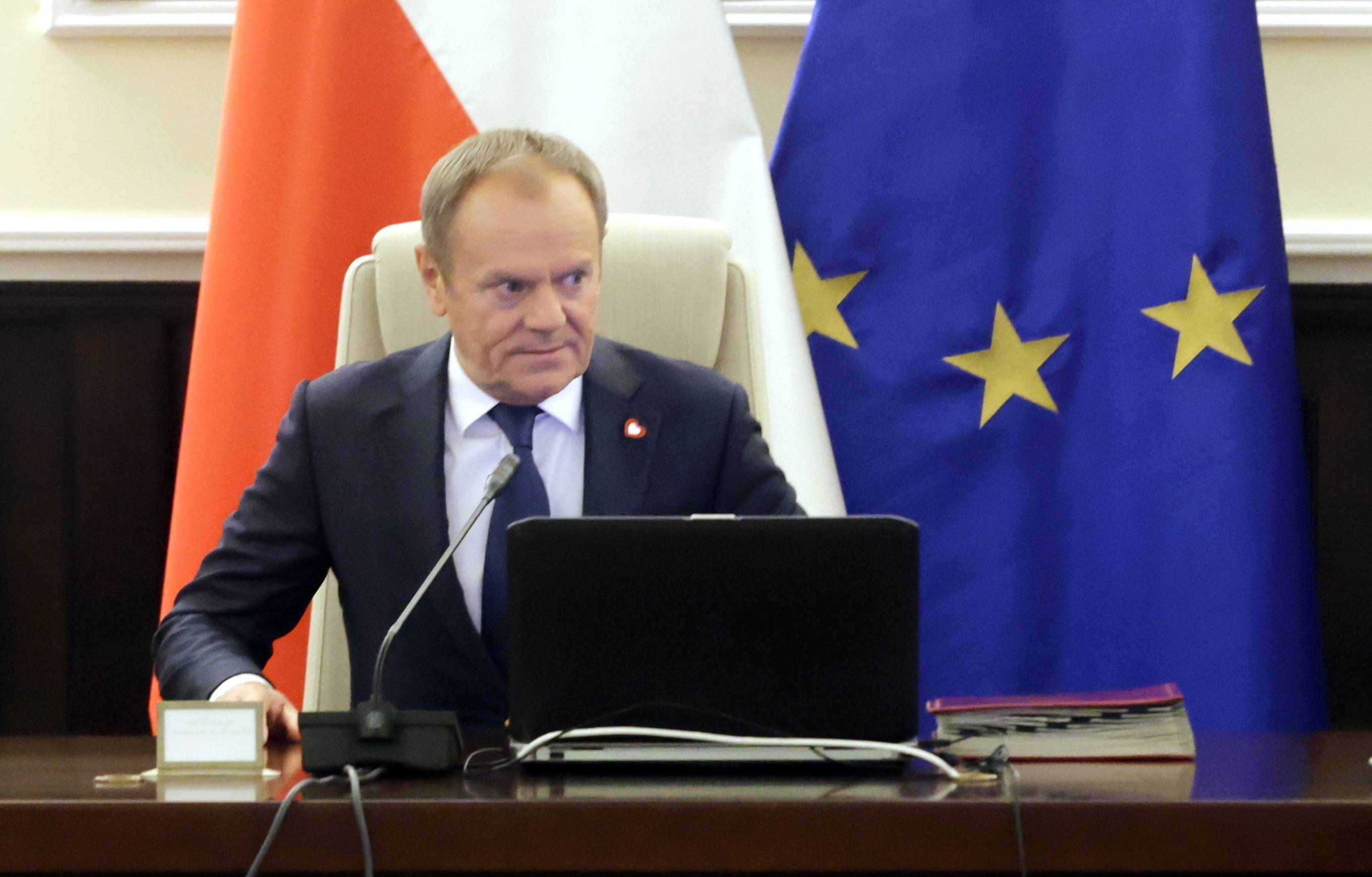 Premier Donald Tusk podczas posiedzenia rządu siedzi na tle flag Polski i Unii Europejskiej