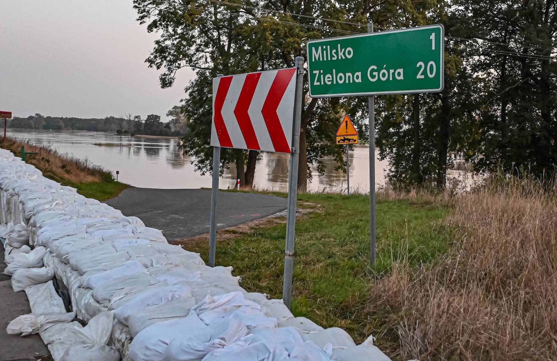 Worki z piaskiem przy wale przeciwpowodziowym oraz tablica pokazująca odległośc od miasta Zielona Góra – 20 km. W tle wezbrany zbiornik