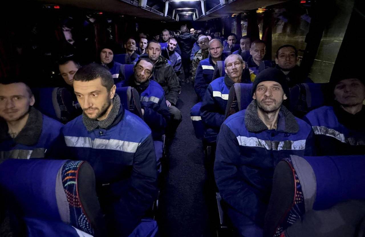 Wychudzeni mężczyźni w jednakowych ciemnych kurtkach siedza w autobusie