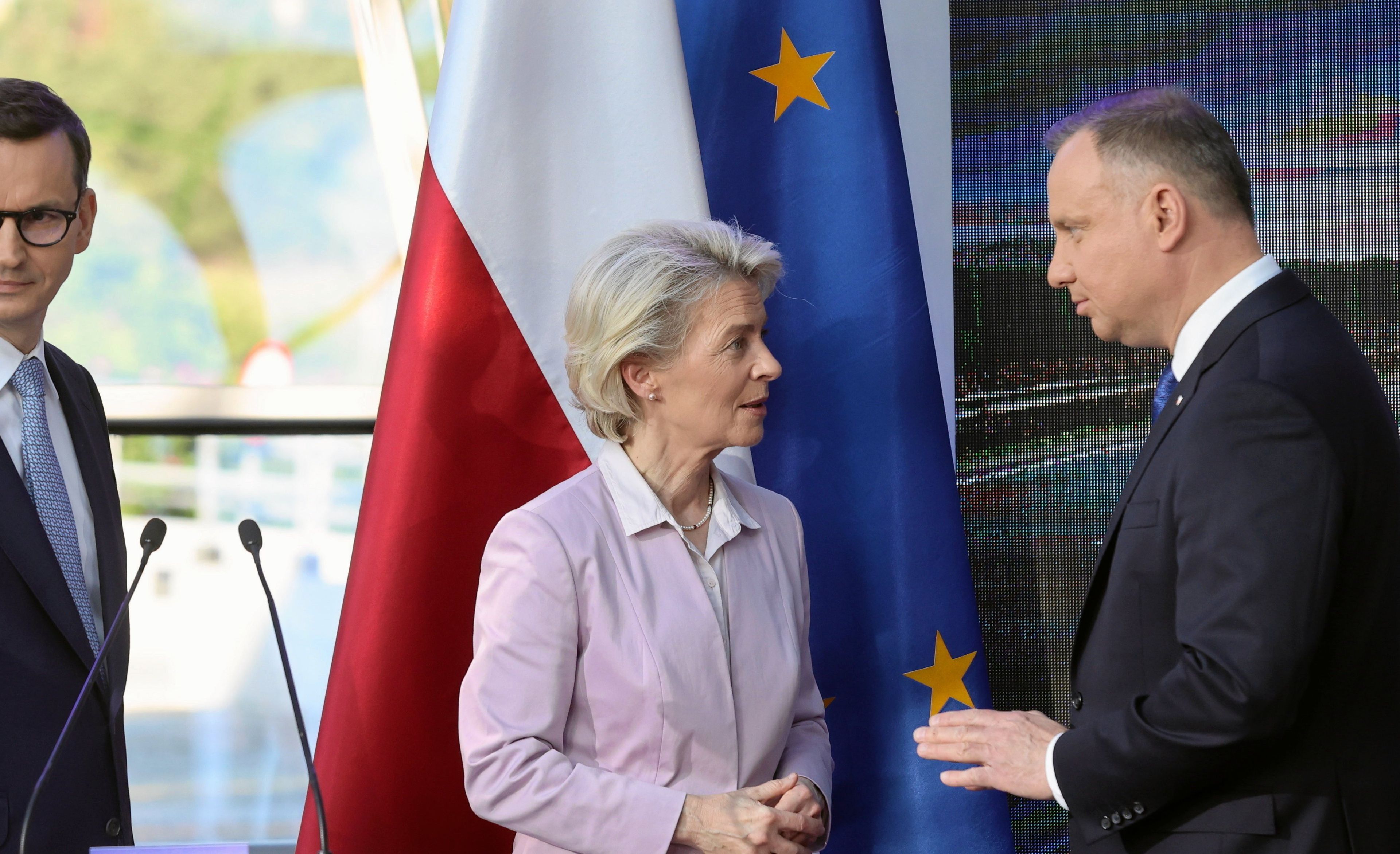 Mateusz Morawiecki, Ursula von Der Leyen i Andrzej Duda rozmawiają przy mównicy. Kobieta stoi w środku, za nimi flagi Unii Europejskiej i Polski