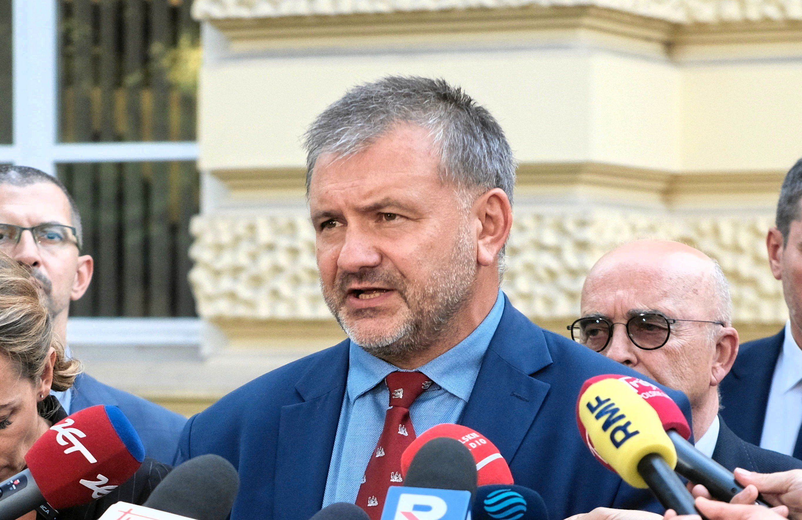 Krótko ostrzyżony mężczyzna w garniturzez odpowiada na pytania dziennikarzy