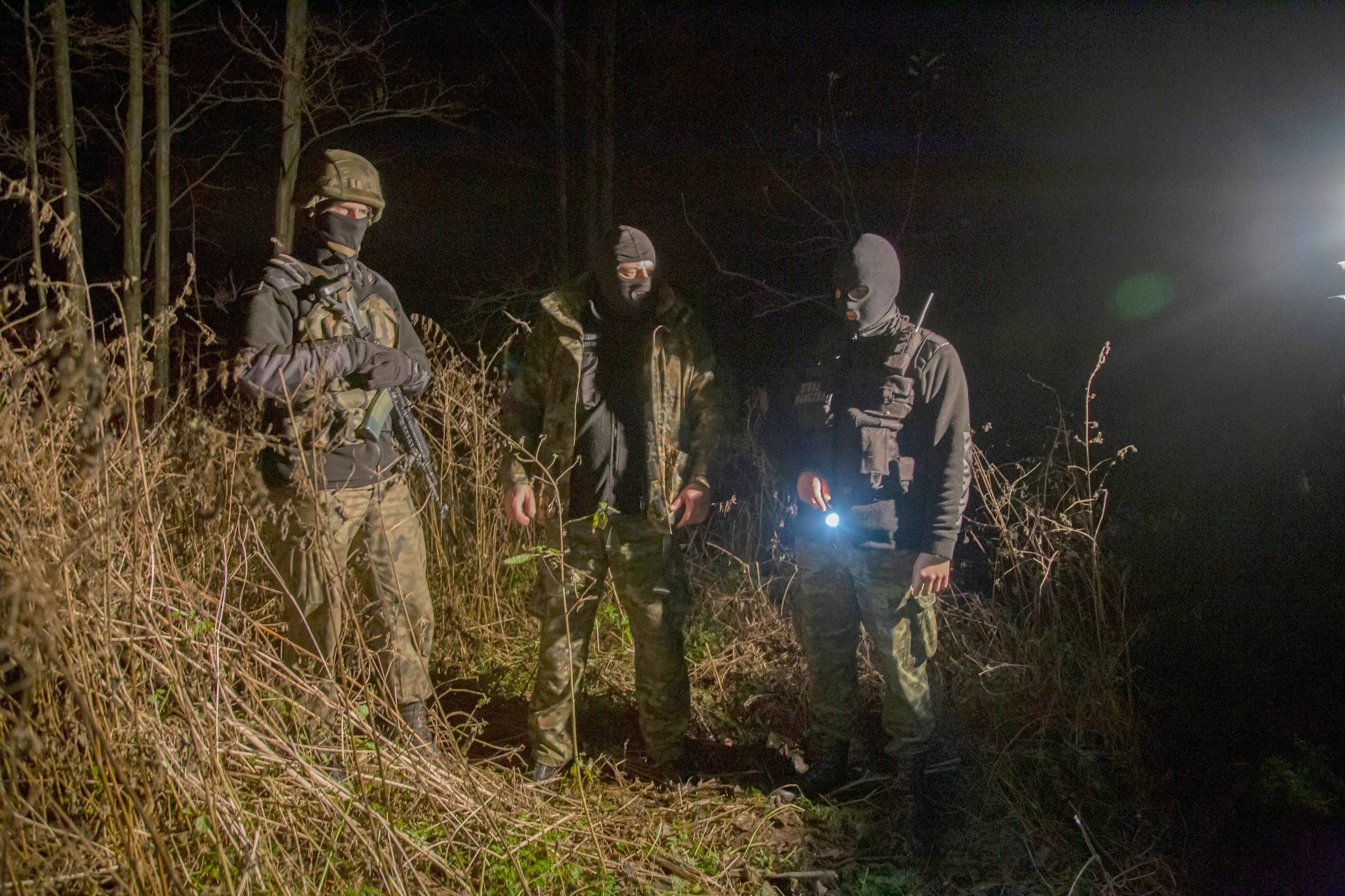 Funkcjonariusze Straży Granicznej świecą latarką w lesie w godzinach nocnych
