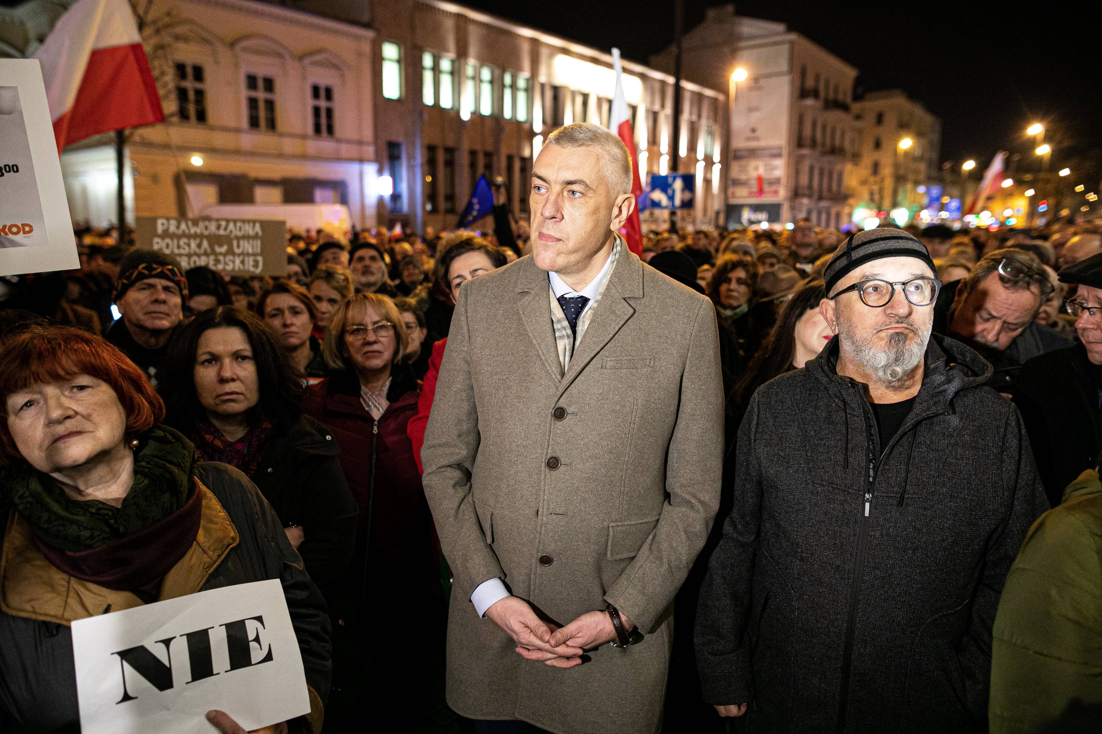 Roman Giertych w jasnym płaszczu stoi na dużym placu, wokół niego kilkudziesięciu ludzi, są ubrani w jesienną odzież