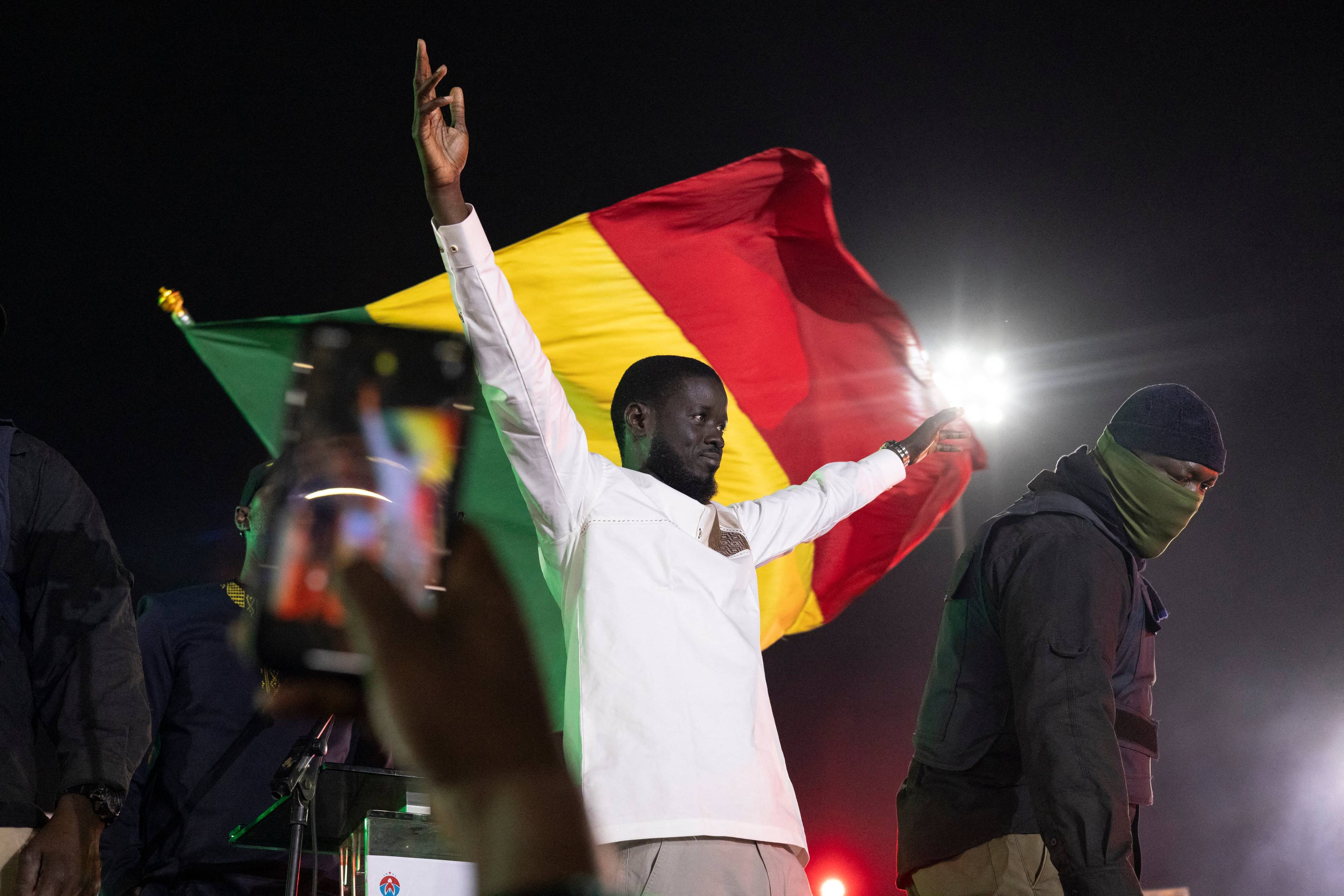 40-letni Afrykanin z rękami do góry w geście tryumfu, z tyłu flaga Senegalu