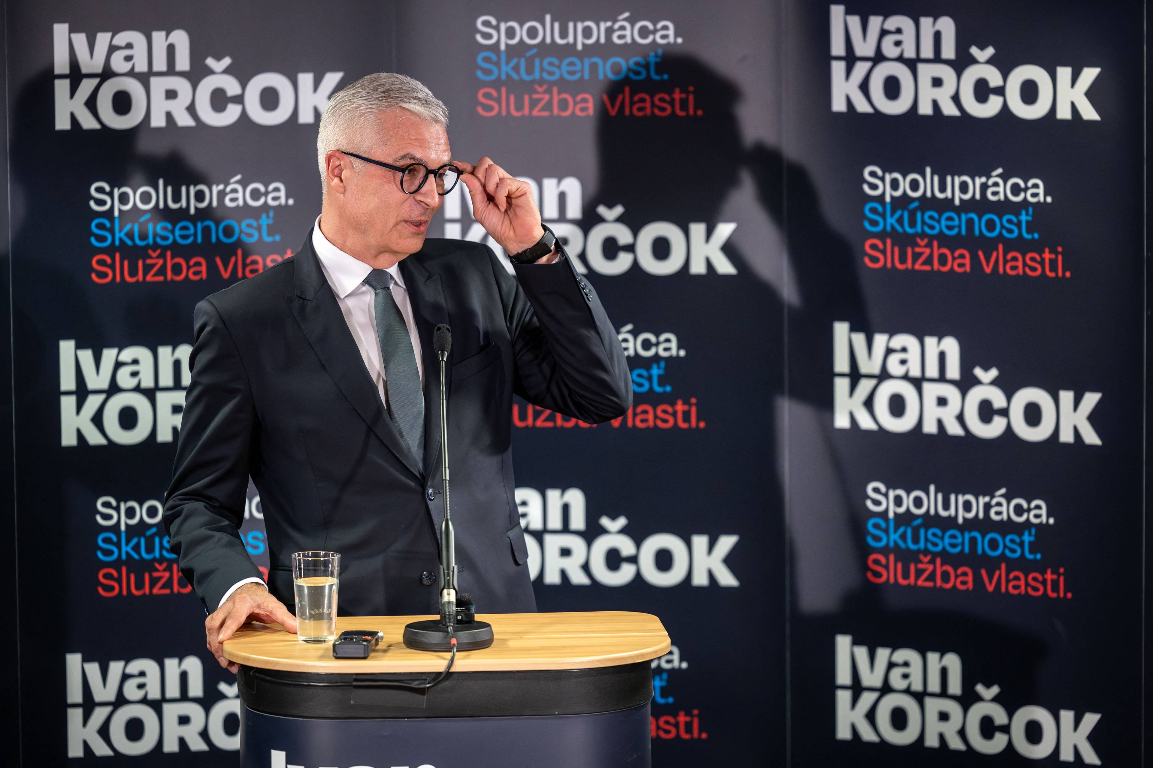 Męzczyzna przemawia na tle plakatów wyborczych z nazwiskiem "Ivan Korcok"