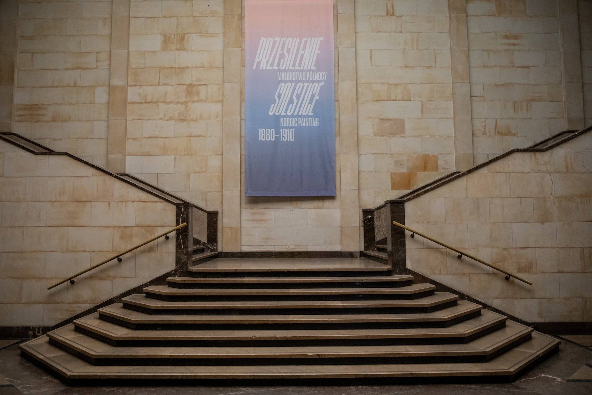 Wnętrze Muzeum Narodowego w Warszawie. Marmurowe schody i plakat reklamujący jedną z wystaw.