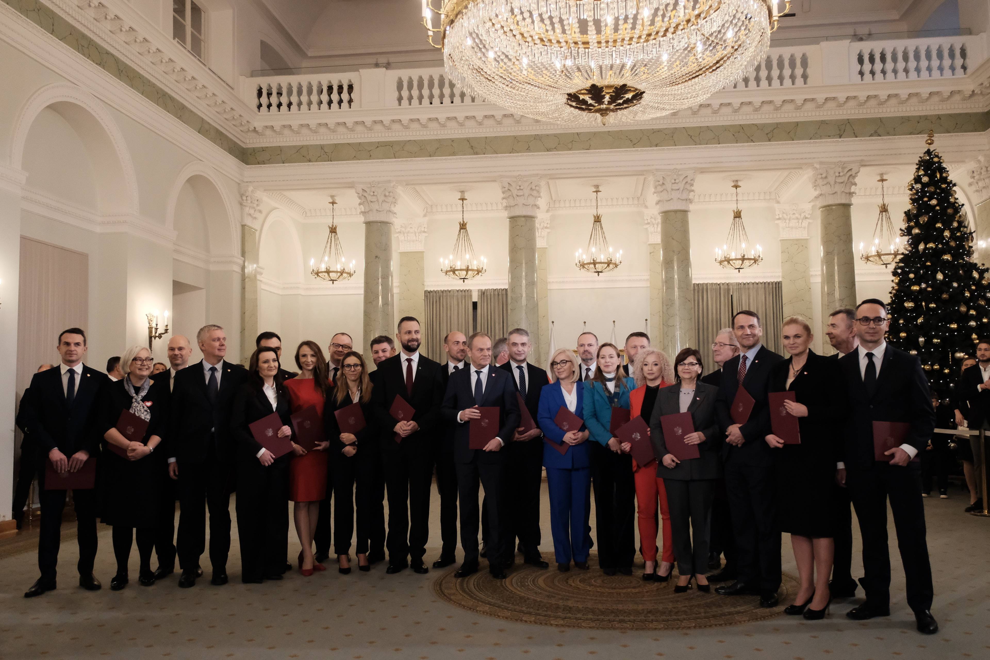 Rząd Tuska: grupowe zdjęcie kobiet i męzczyzn pod zyrandolem w pałacu prezydenckim