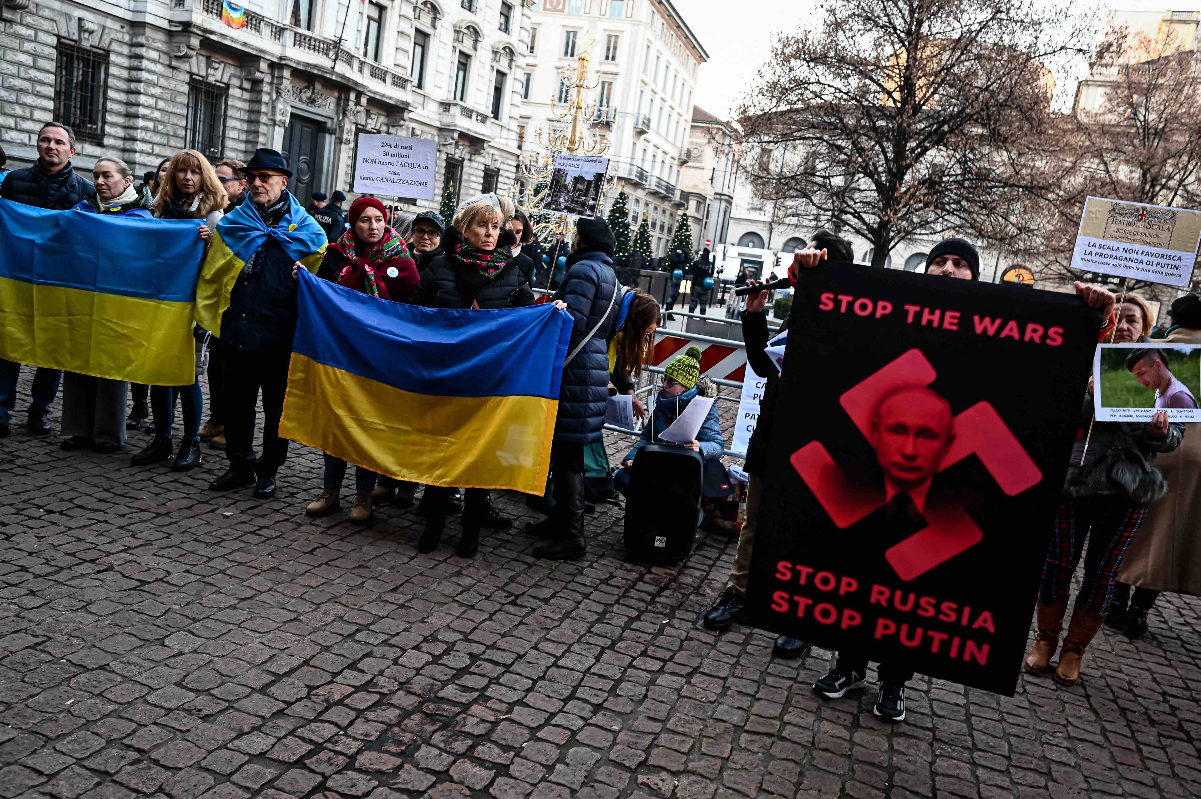 Protestujący na ulicy trzymają ukraińskie flagi oraz plakat z twarzą Putina wpisaną w czerwoną swastykę na czarnym tle i napisem Stop War - Stop wojnie. Rosjanie