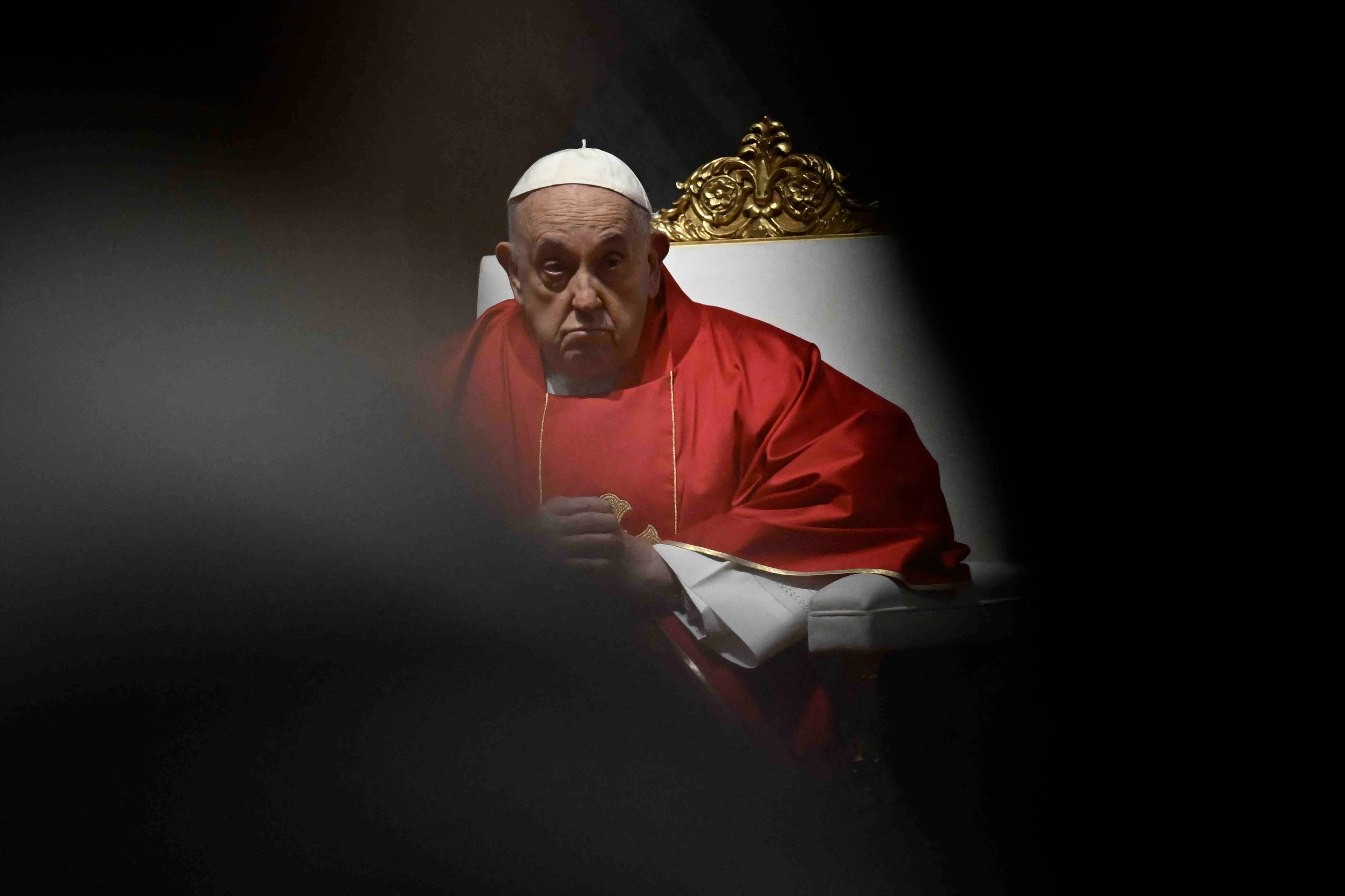 Papież w czerwonej szacie i białym birecie siedzi na fotelu podczas mszy.