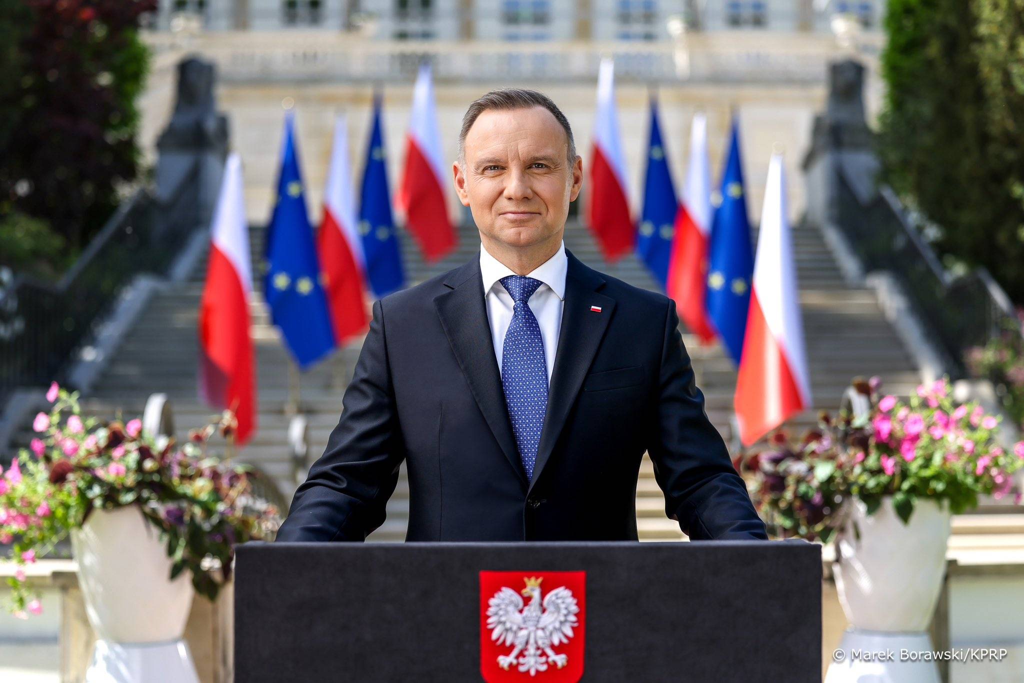 na zdjęciu prezydent Andrzej Duda przemawia przed Pałacem, dzień jest pogodny, słoneczny. Za nim widać polskie i unijne flagi