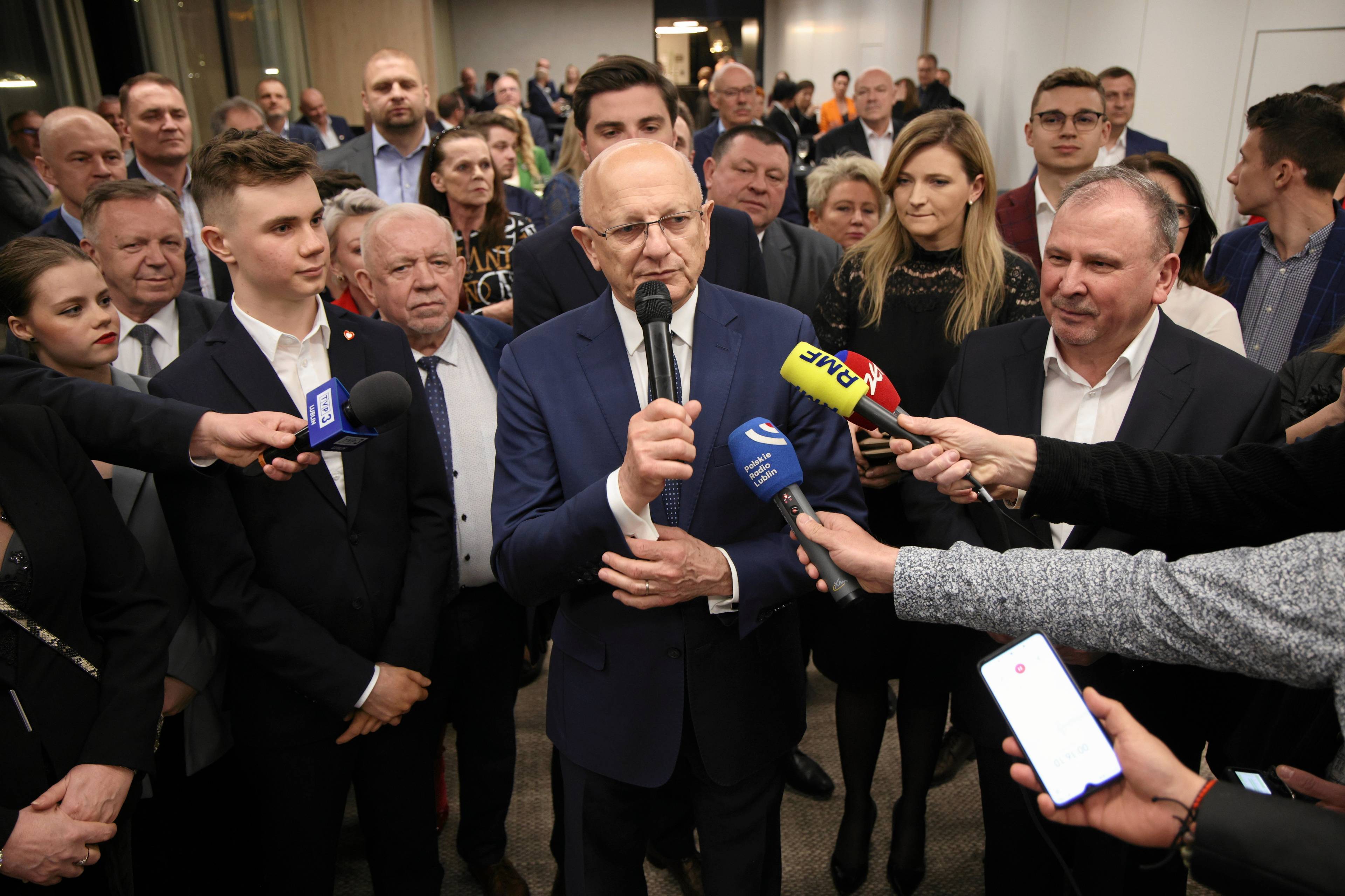 Mężczyzna w otoczeniu grupy osób odpowiada na pytania dziennikarzy. Województwo lubelskie - wybory