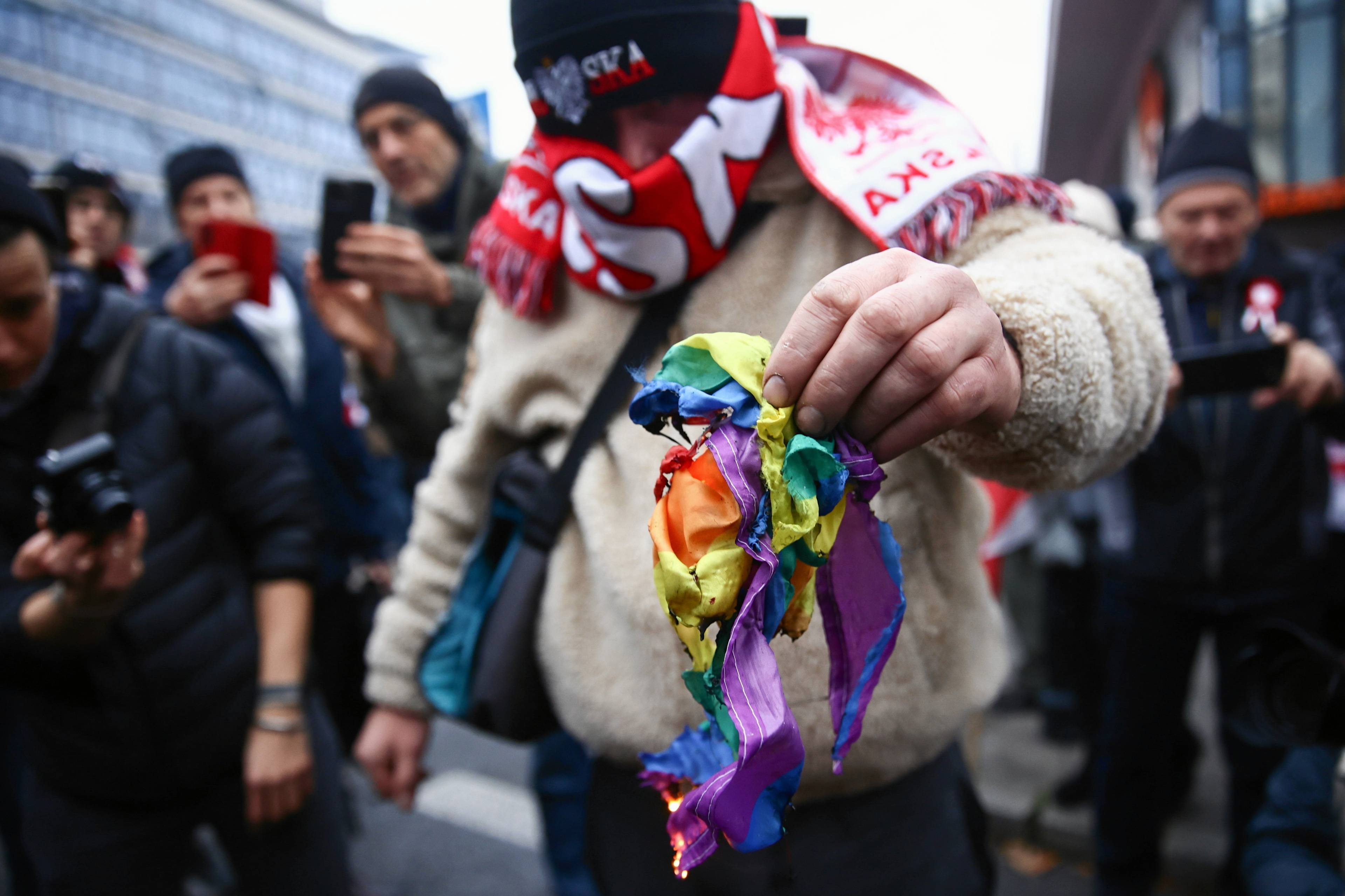 Uczestnik Marszu Niepodległości w Warszawie pali tęczową flagę, symbol społeczności LGBT+