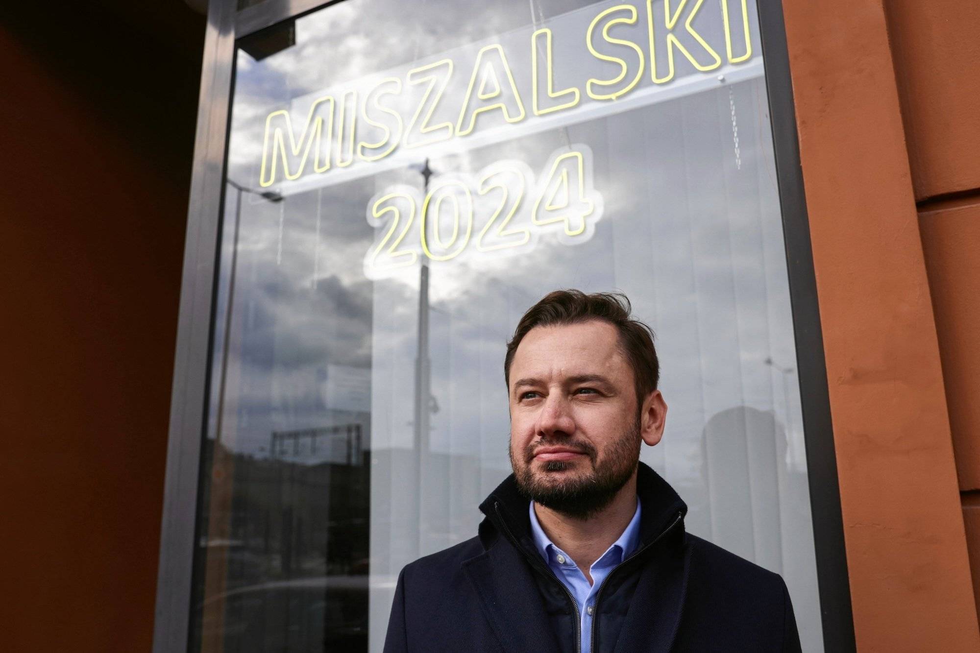 Aleksander Miszalski na tle swojego neonu wyborczego w 2024 roku.