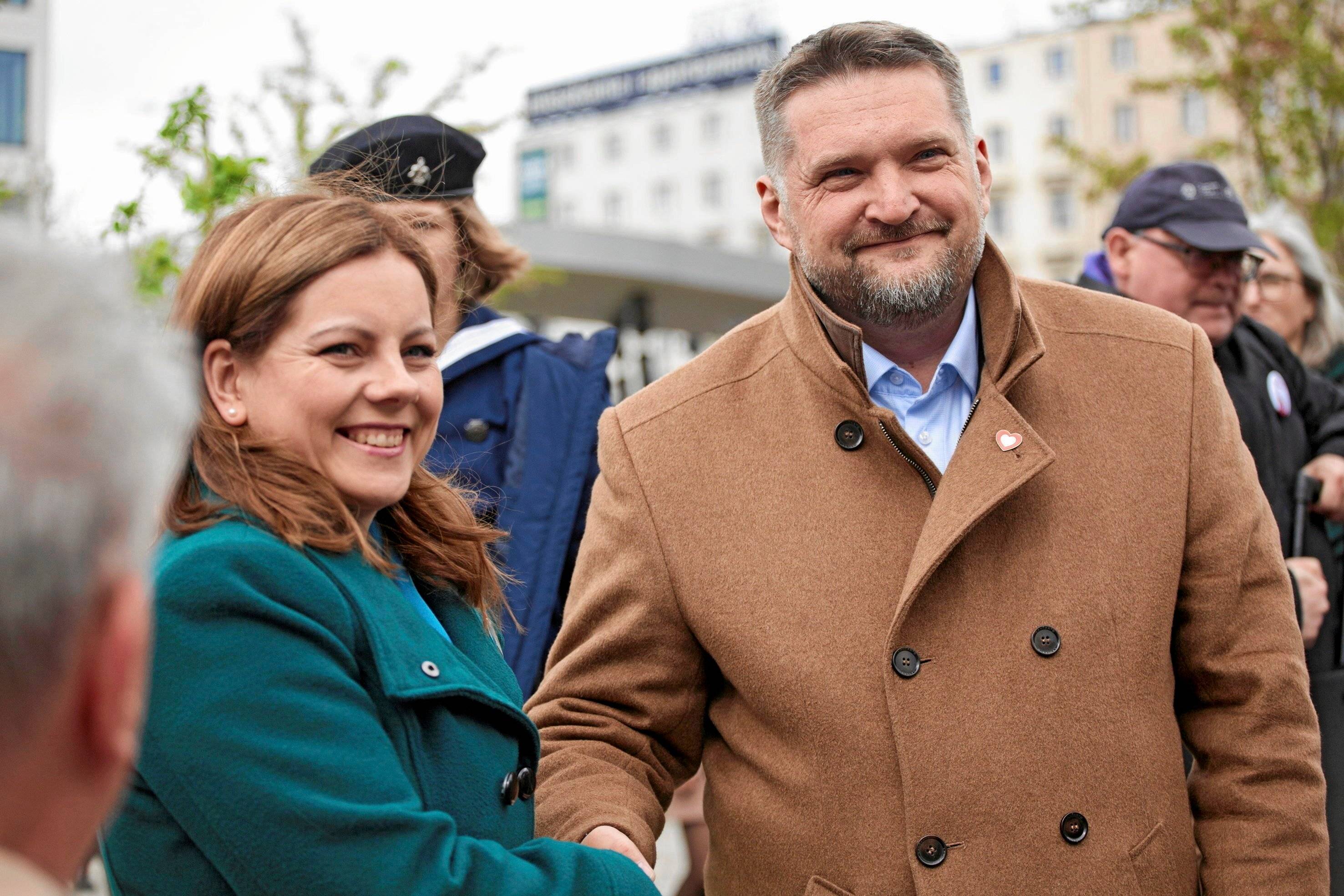 Kandydaci na prezydenta Gdyni Aleksandra Kosiorek i Tadeusz Szemiot stoją obok siebie na ulicy i podaja sobie ręce. Gdynia